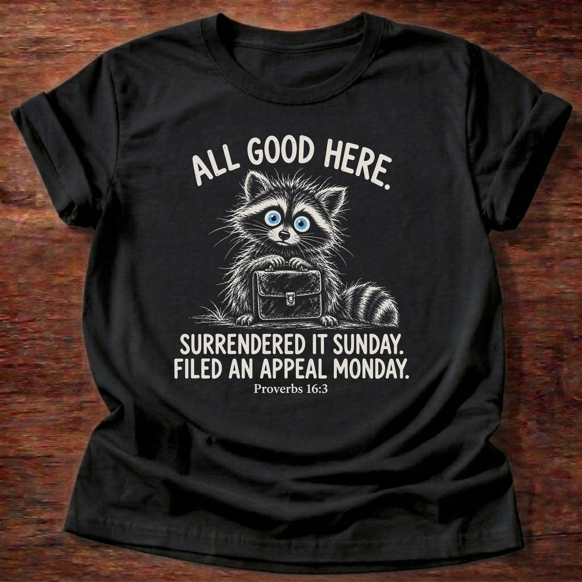 Black t-shirt printed with a raccoon carrying a briefcase graphic and “All good here. Surrendered it Sunday. Filed an appeal Monday.” Proverbs 16:3 Christian shirt