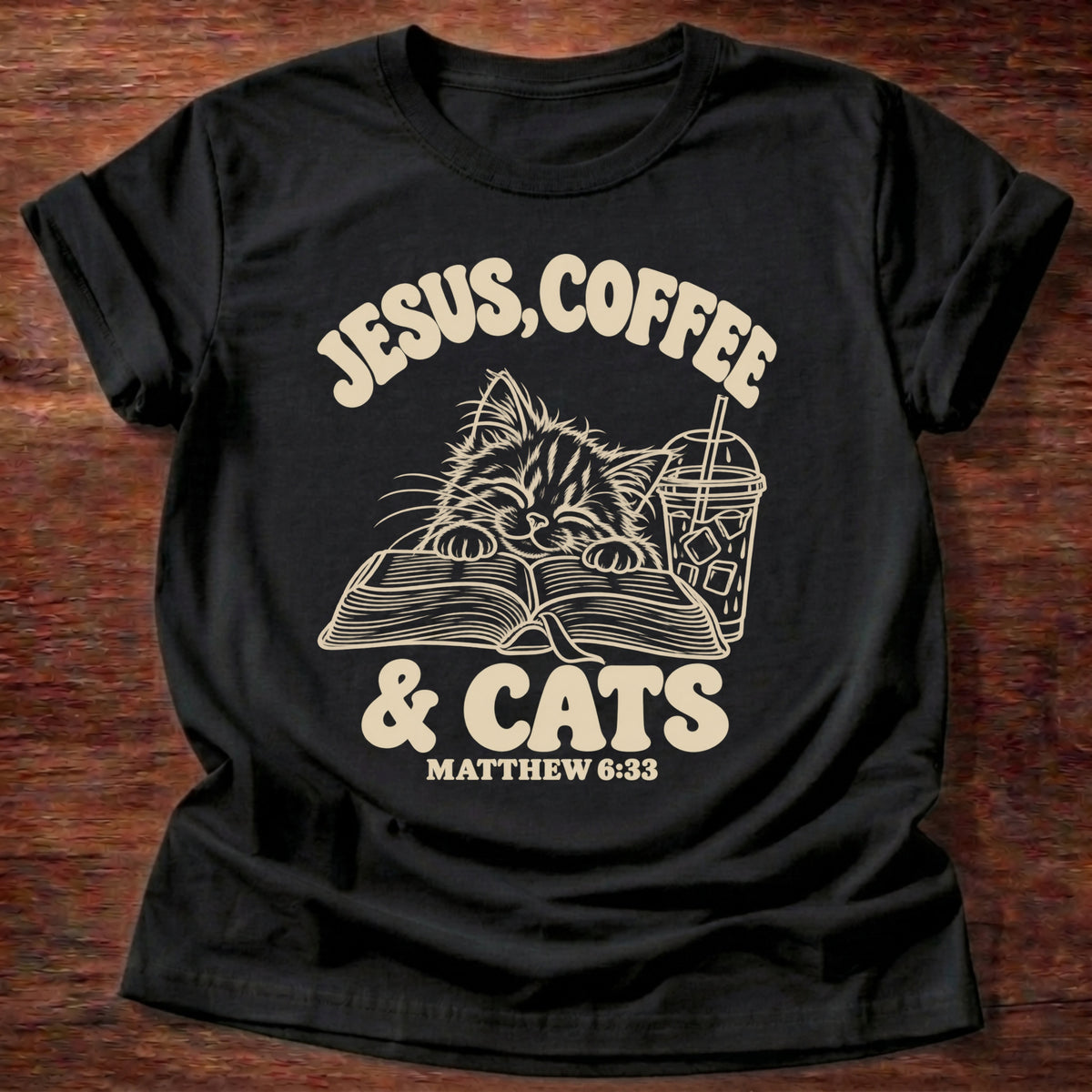 Black t-shirt printed with a kitten reading an open Bible beside an iced coffee and “Jesus, Coffee & Cats” Matthew 6:33 Christian shirt
