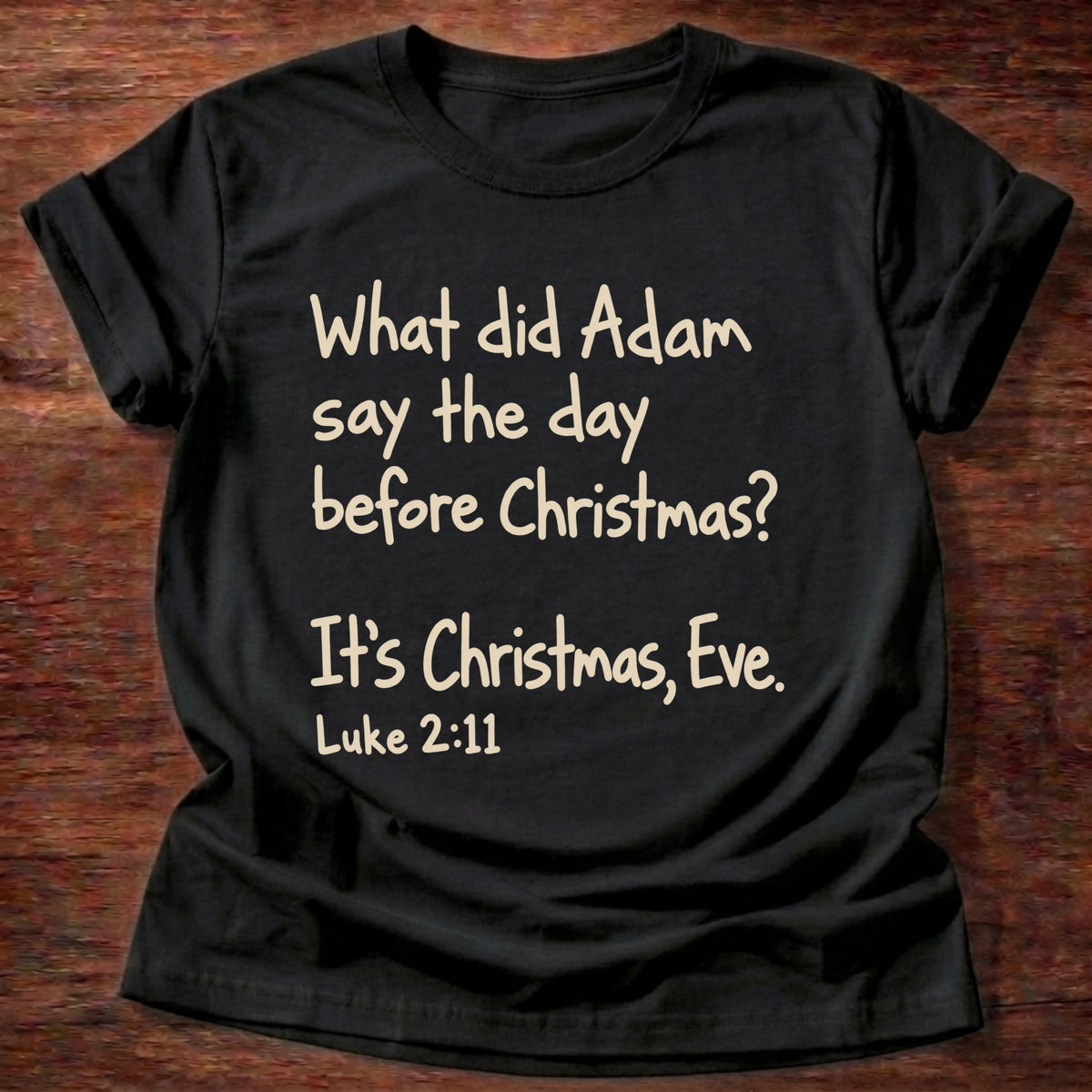Black t-shirt printed with a simple hand-lettered Bible joke graphic and “What did Adam say the day before Christmas? It's Christmas, Eve.” Luke 2:11 Christian shirt