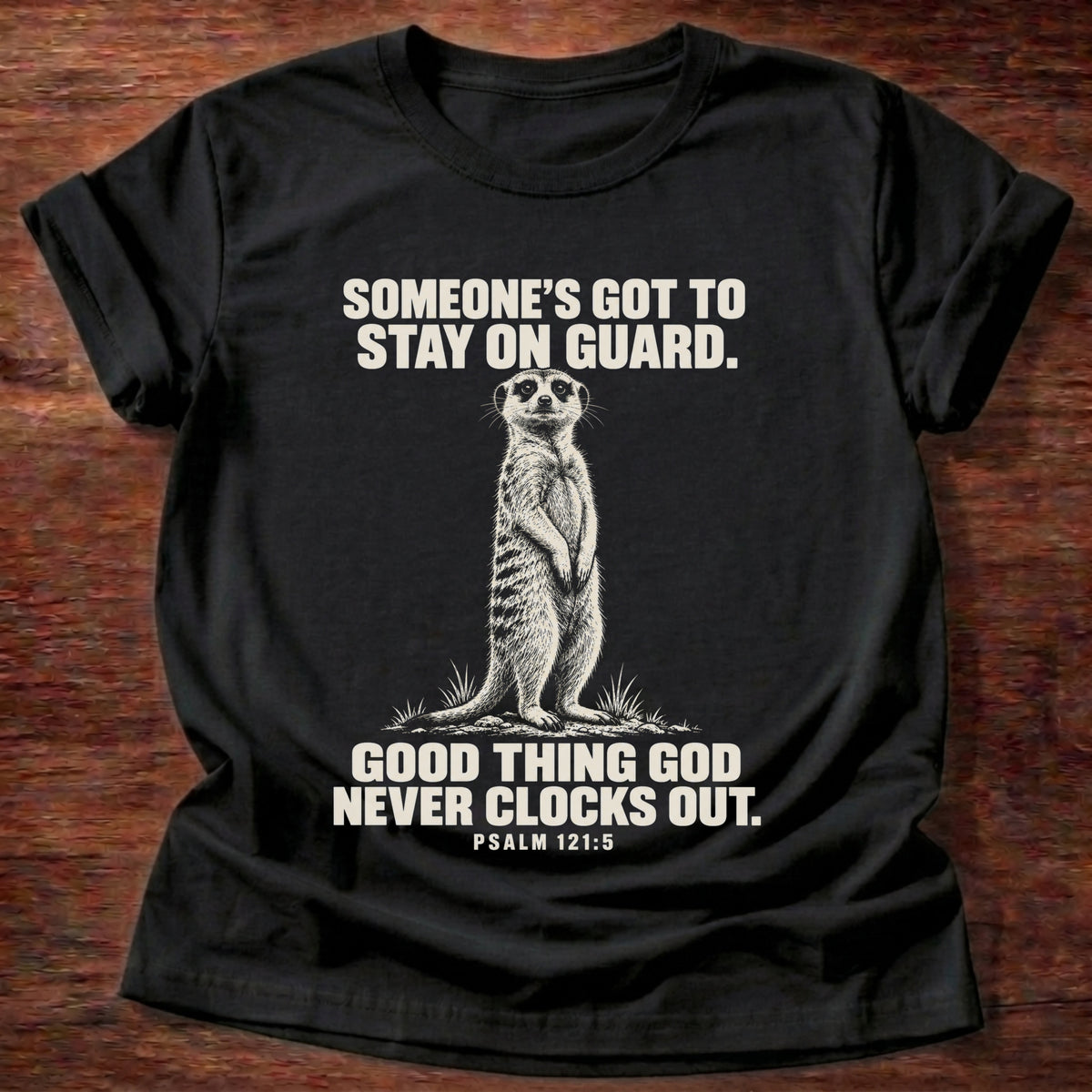 Black t-shirt printed with a meerkat standing guard on lookout graphic and 'Someone's got to stay on guard. Good thing God never clocks out.' Psalm 121:5 faith based gift
