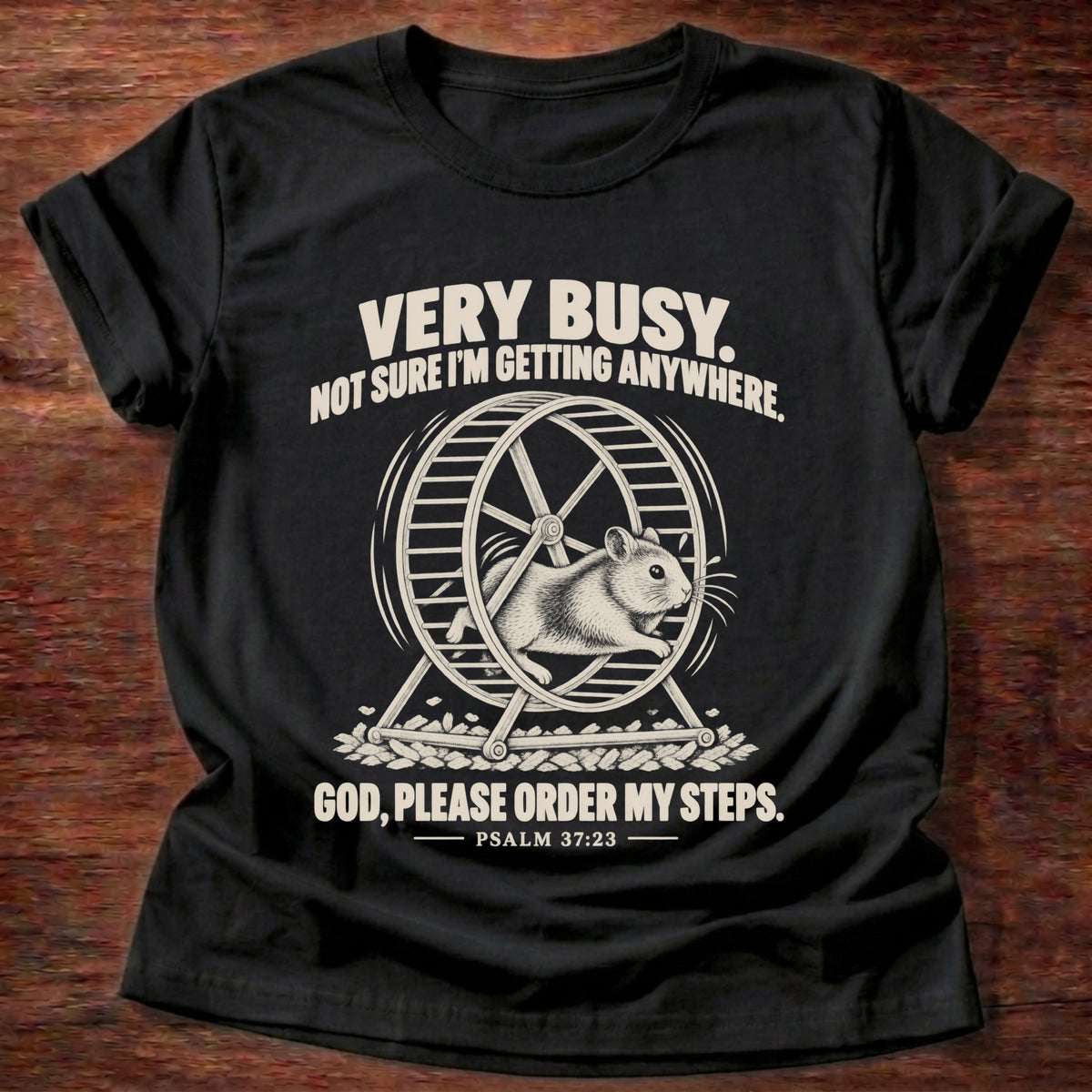 Black t-shirt printed with a squirrel running on a wheel graphic and 'Very busy. Not sure I'm getting anywhere. God, please order my steps.' Psalm 37:23 faith based gift