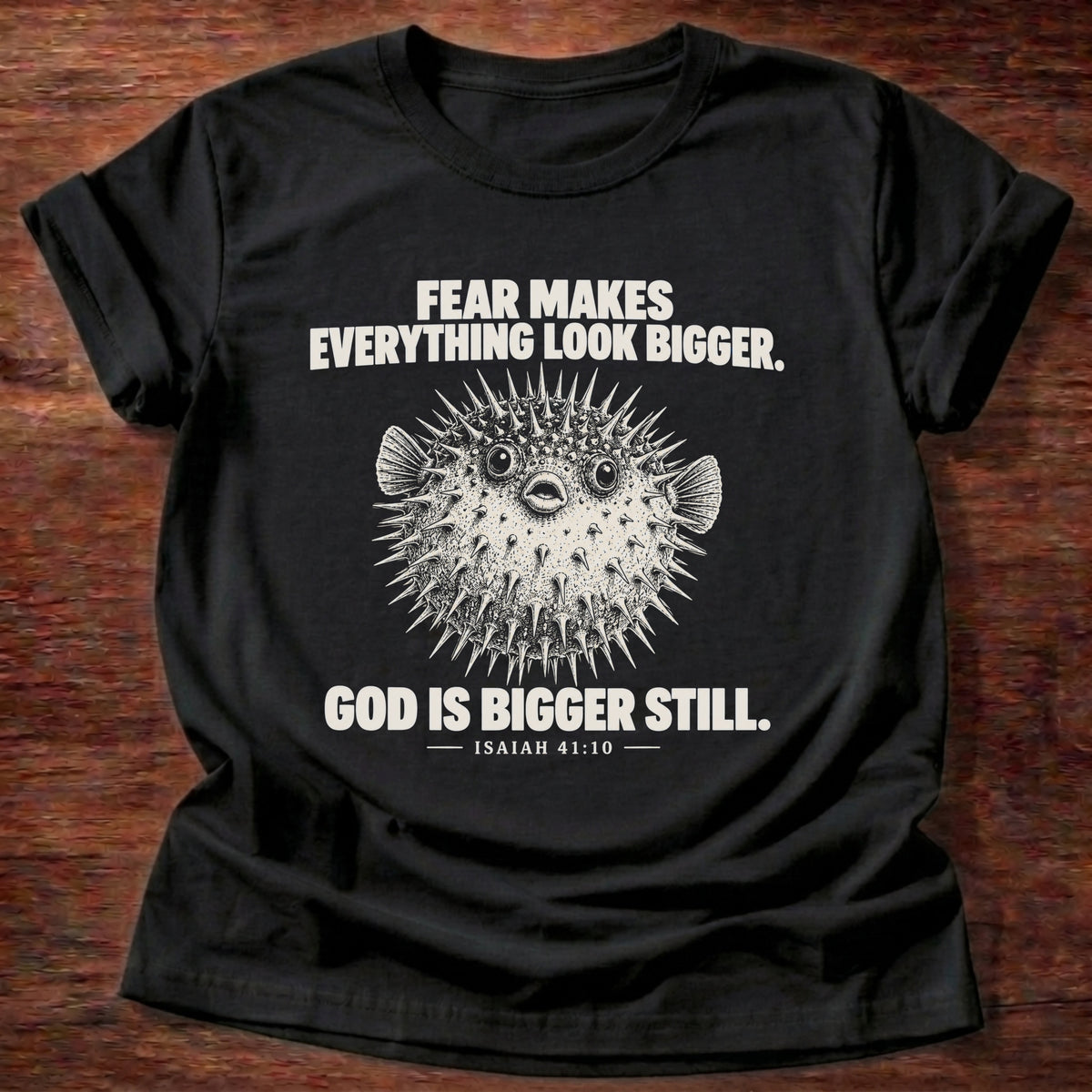 Black t-shirt printed with a pufferfish inflated to look bigger graphic and 'Fear makes everything look bigger. God is bigger still.' Isaiah 41:10 faith based gift