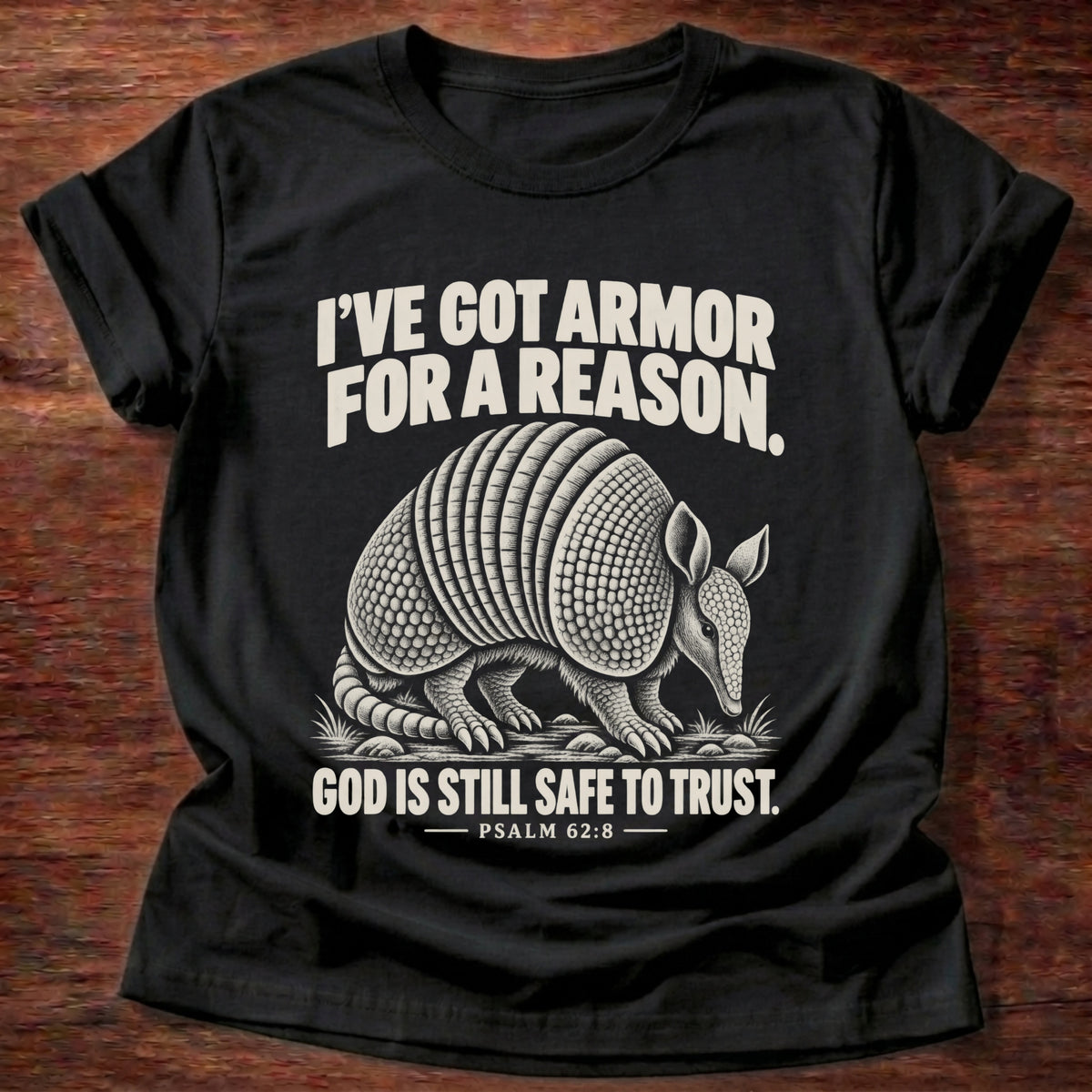 Black t-shirt printed with an armadillo in full armor graphic and 'I've got armor for a reason. God is still safe to trust.' Psalm 62:8 faith based gift