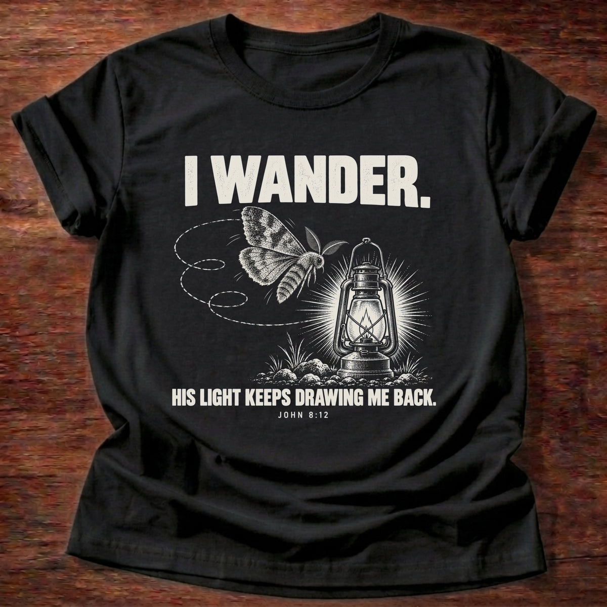 Black t-shirt printed with a moth circling a glowing lantern graphic and 'I wander. His light keeps drawing me back.' John 8:12 faith based gift