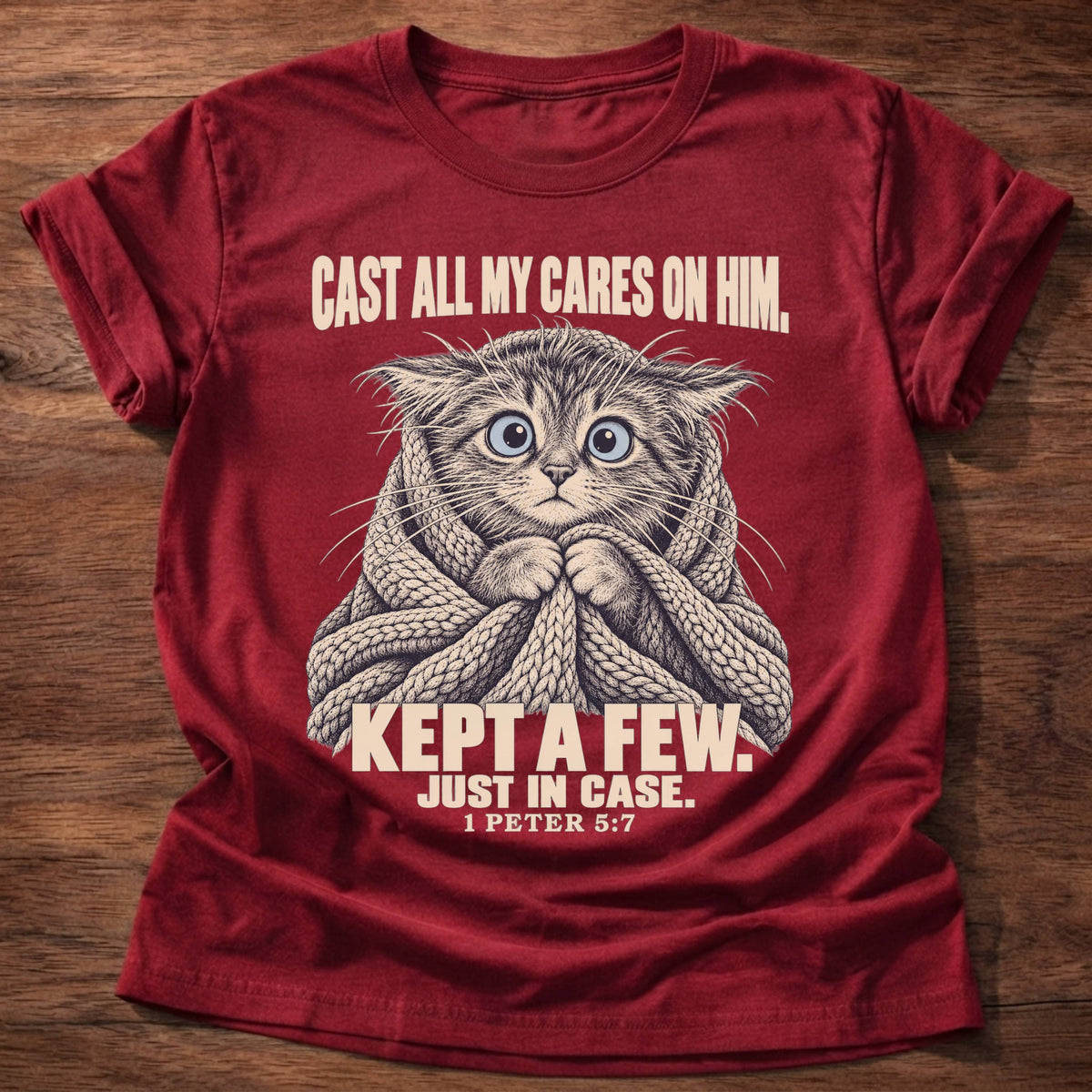 Kept A Few T-Shirt in Cherry Red featuring a wide-eyed cat wrapped in a knit blanket and 1 Peter 5:7 anxiety humor design
