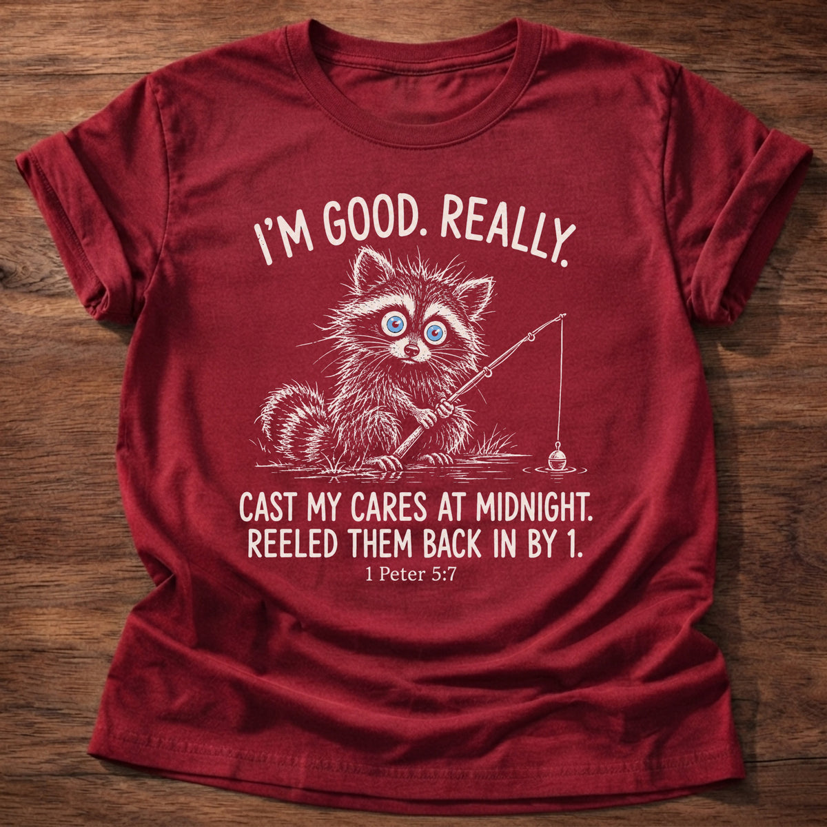 Cherry Red t-shirt printed with a raccoon holding a fishing rod graphic and “I'm good. Really. Cast my cares at midnight. Reeled them back in by 1.” 1 Peter 5:7 Christian shirt