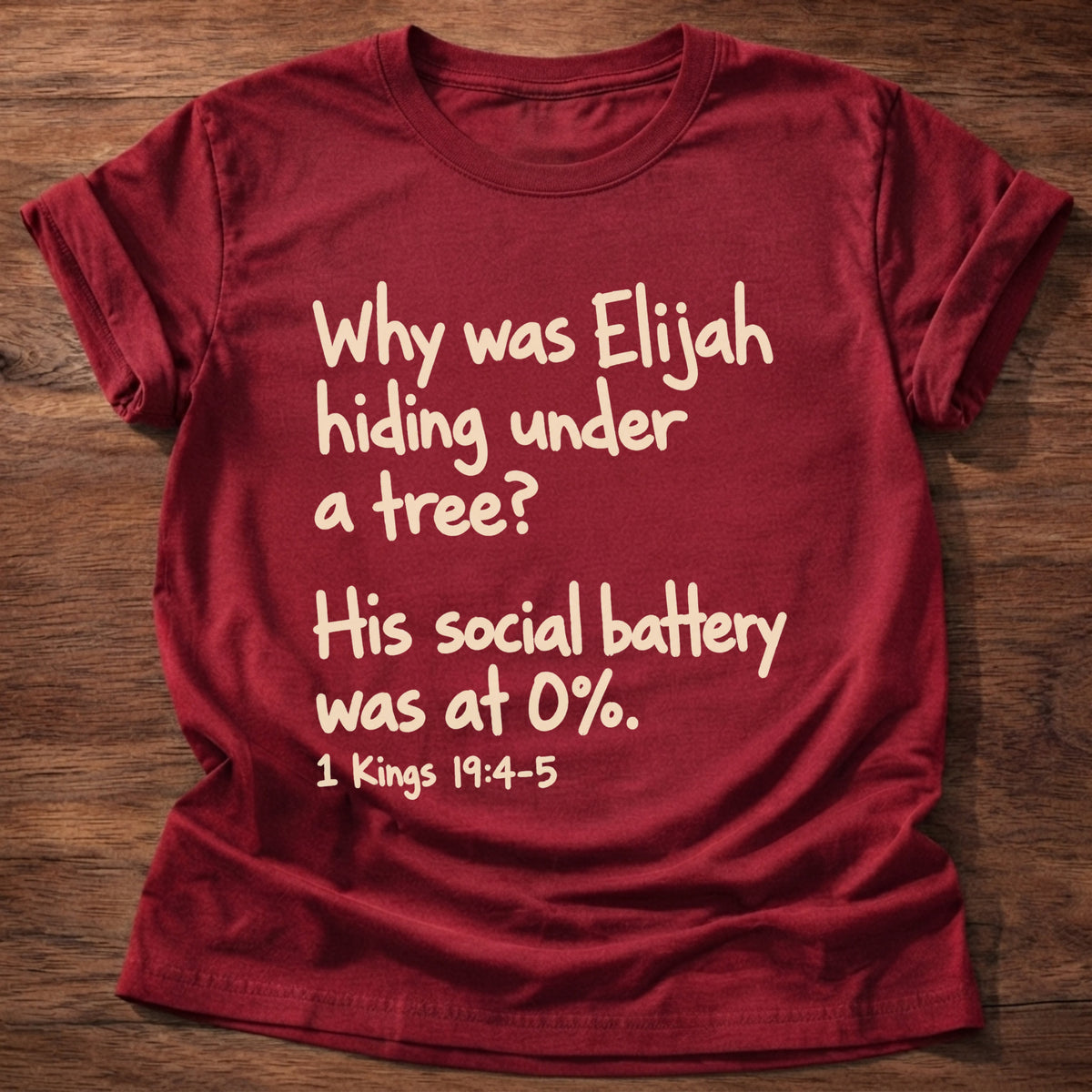 Cherry Red t-shirt printed with a simple hand-lettered Bible joke graphic and “Why was Elijah hiding under a tree? His social battery was at 0%.” 1 Kings 19:4-5 Christian shirt