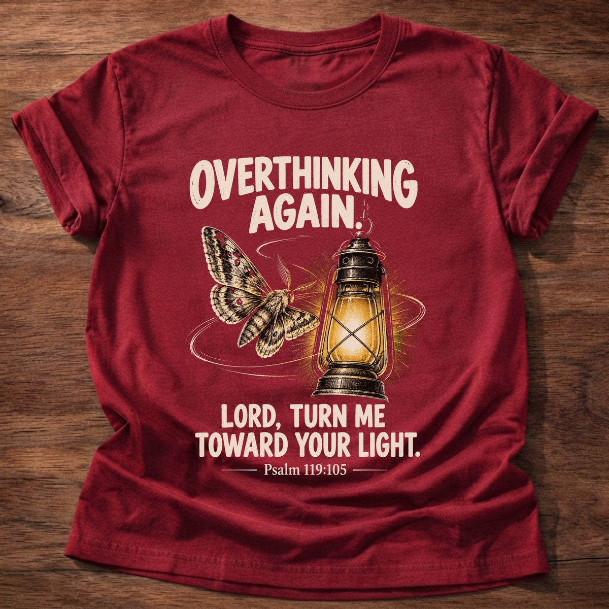Cherry Red t-shirt printed with a moth drawn toward a glowing vintage lantern graphic and “Overthinking again. Lord, turn me toward Your light.” Psalm 119:105 faith based gift