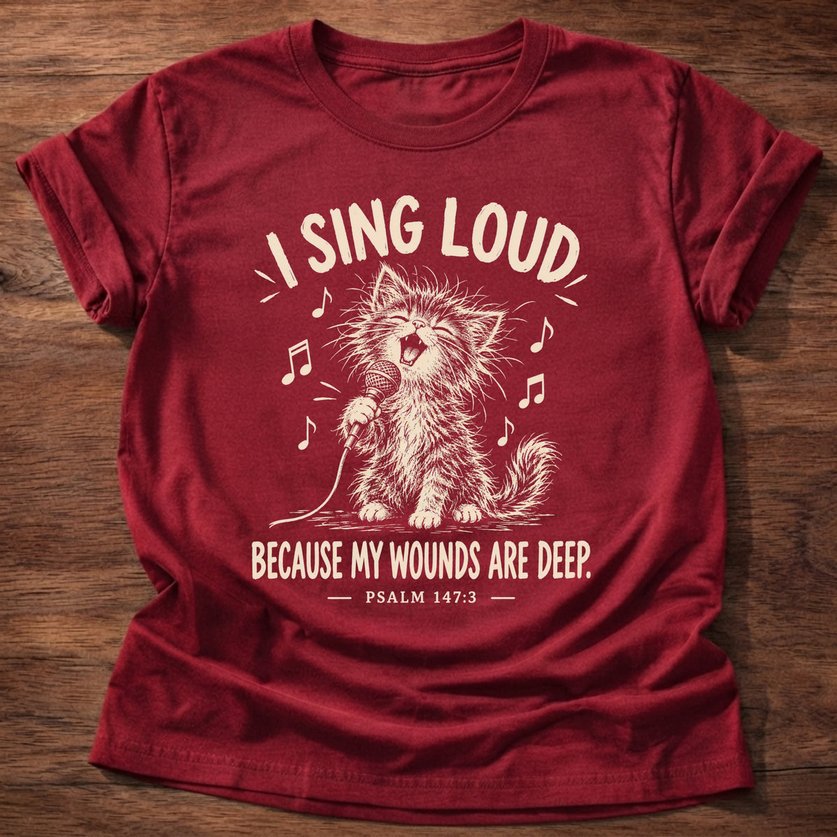 Sing Loud T-Shirt in Cherry Red featuring a kitten singing into a microphone and Psalm 147:3 worship and healing design