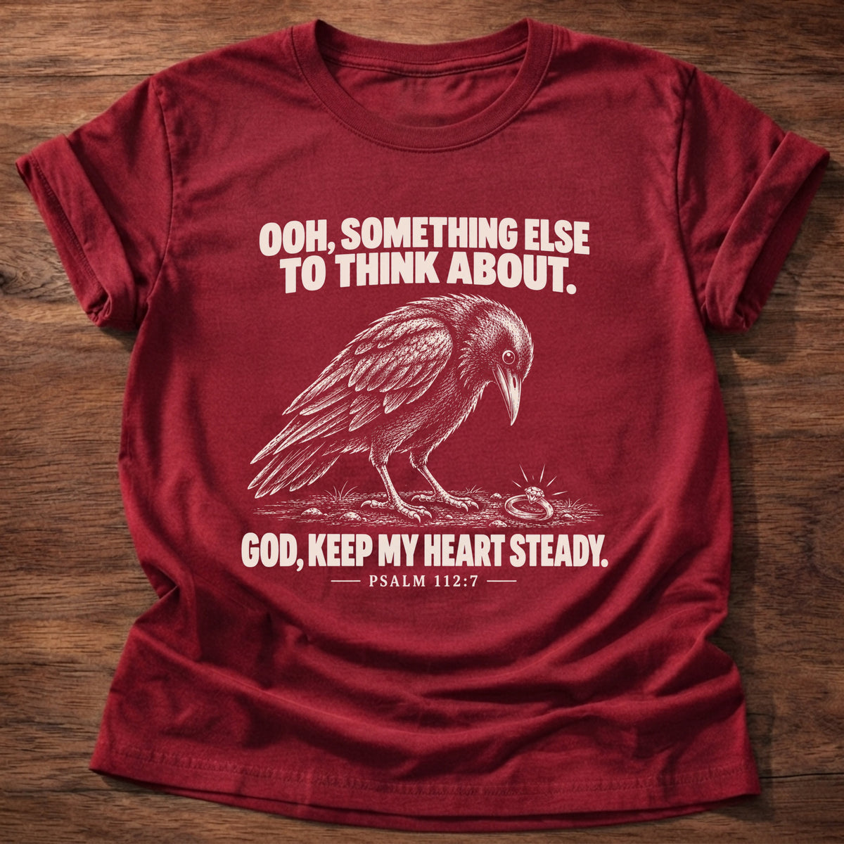 Cherry Red t-shirt printed with a crow investigating something shiny on the ground graphic and 'Ooh, something else to think about. God, keep my heart steady.' Psalm 112:7 faith based gift