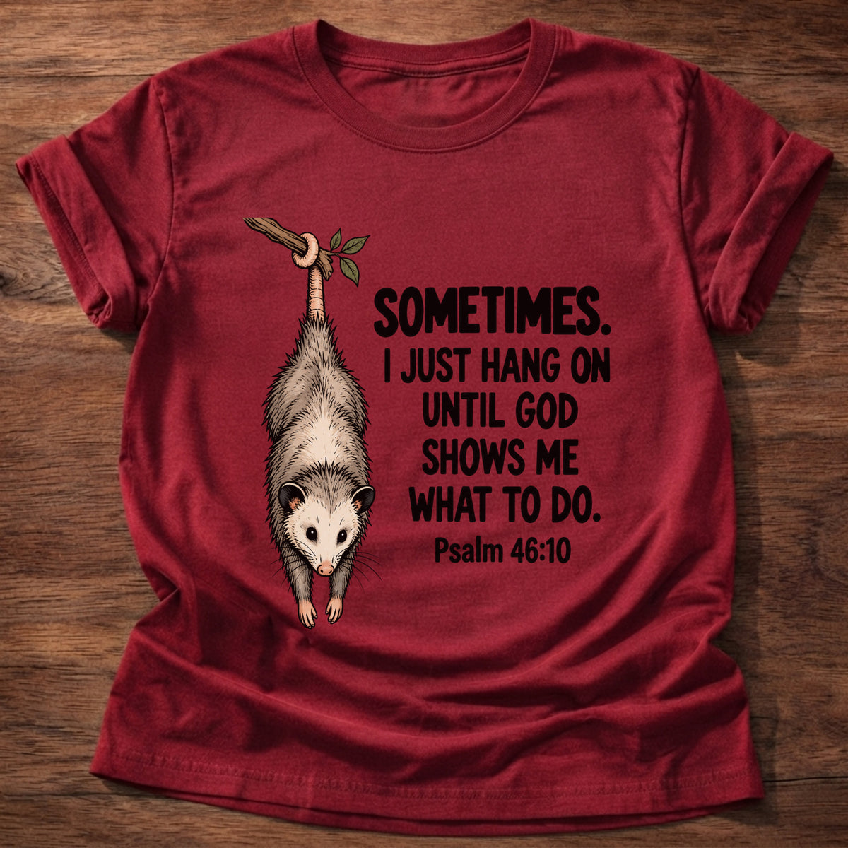Cherry Red t-shirt printed with a possum hanging by its tail graphic and 'Sometimes. I just hang on until God shows me what to do.' Psalm 46:10 faith based gift