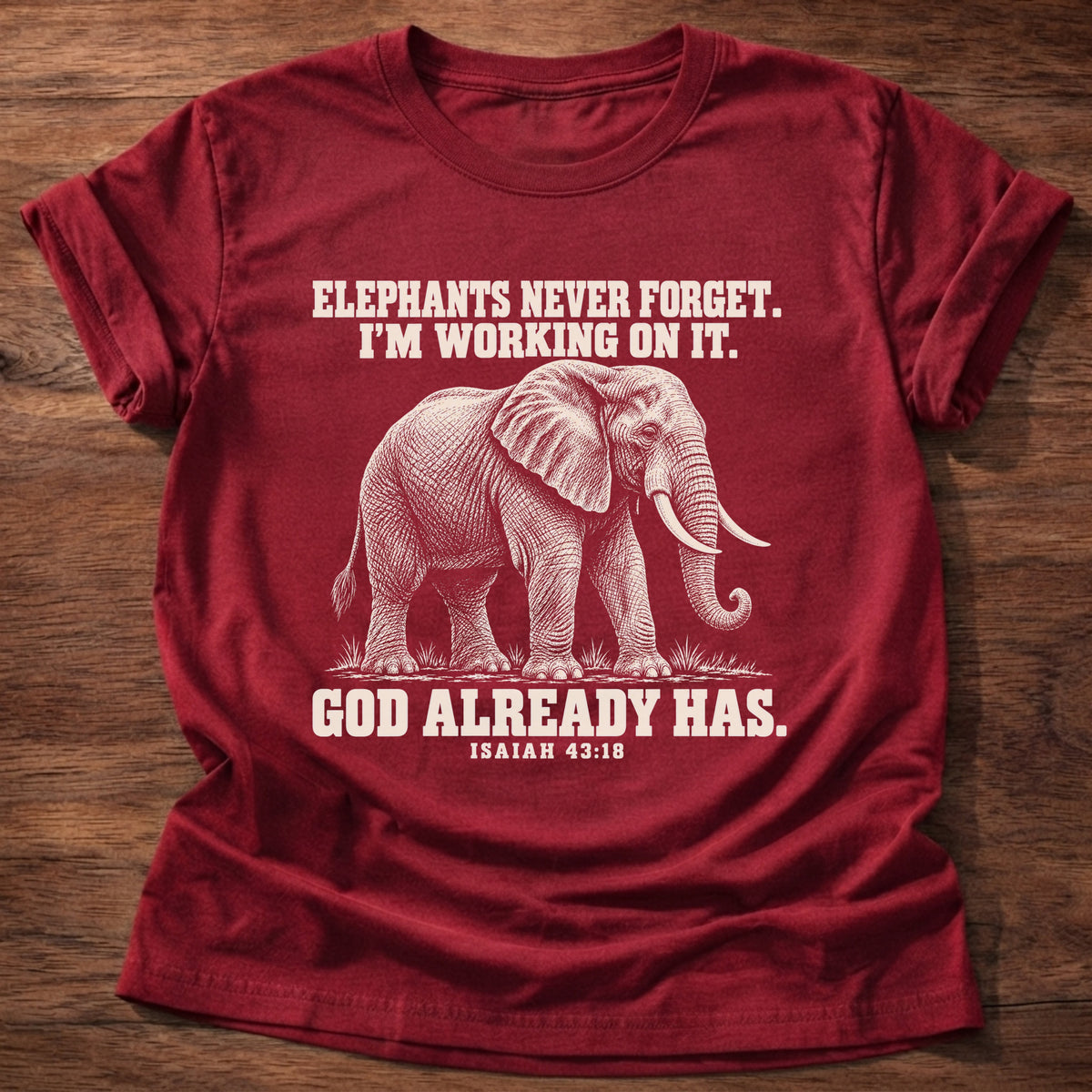Cherry Red t-shirt printed with an elephant walking through tall grass graphic and 'Elephants never forget. I'm working on it. God already has.' Isaiah 43:18 faith based gift