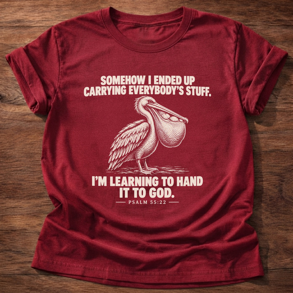 Cherry Red t-shirt printed with a pelican with a pouch full of fish graphic and 'Somehow I ended up carrying everybody's stuff. I'm learning to hand it to God.' Psalm 55:22 faith based gift