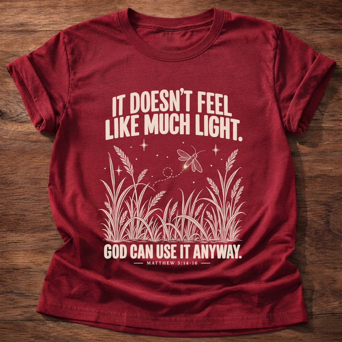 Cherry Red t-shirt printed with a firefly glowing in a dark field of grass graphic and 'It doesn't feel like much light. God can use it anyway.' Matthew 5:14-16 faith based gift