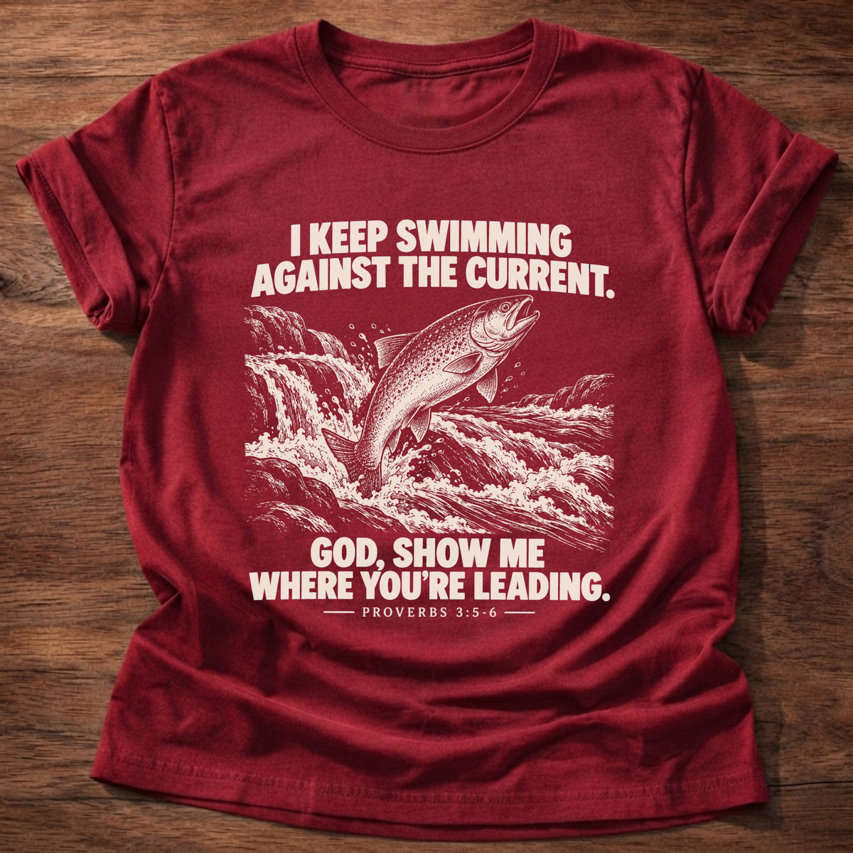 Cherry Red t-shirt printed with a fish leaping against a rushing current graphic and 'I keep swimming against the current. God, show me where you're leading.' Proverbs 3:5-6 faith based gift