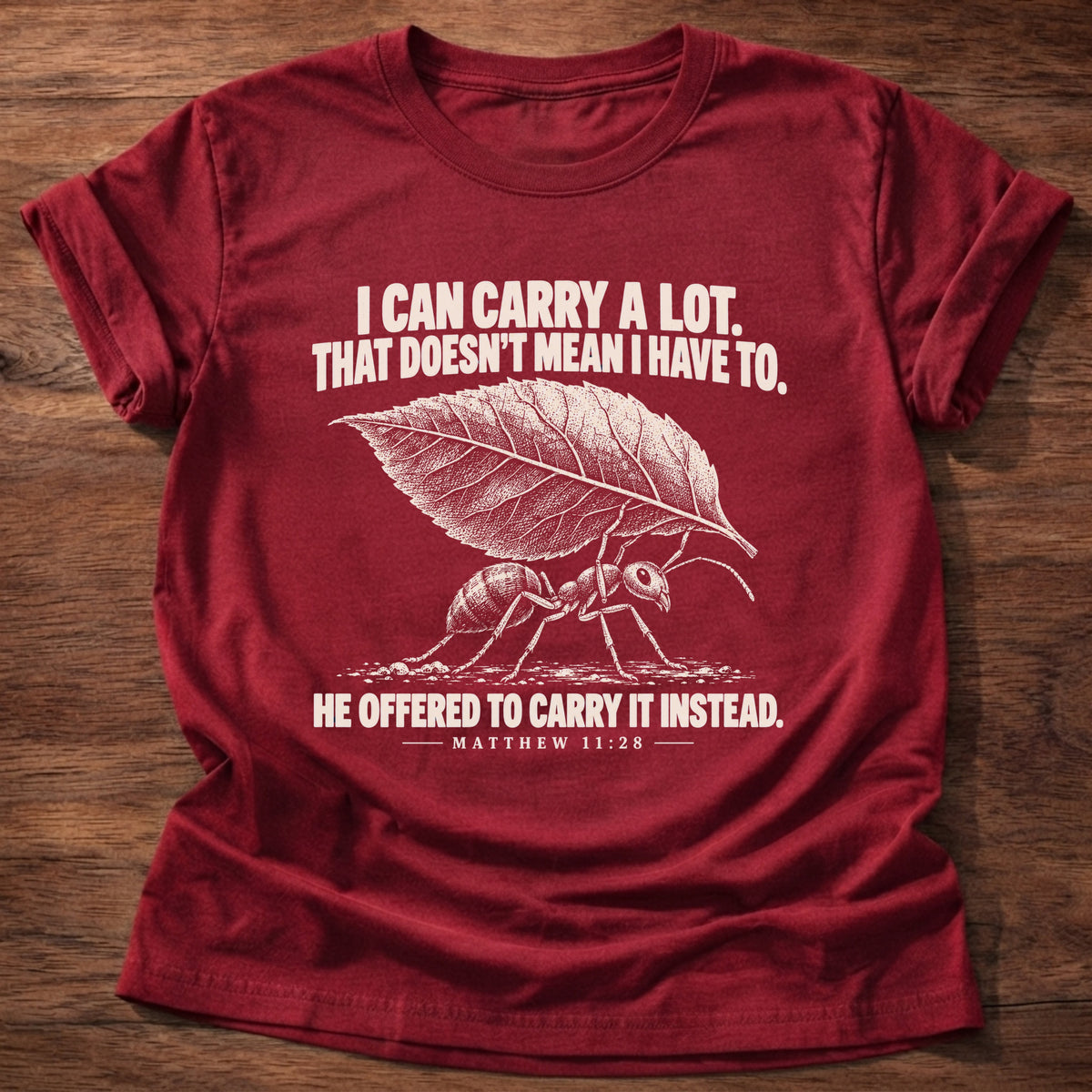 Cherry Red t-shirt printed with an ant hauling a leaf many times its size graphic and 'I can carry a lot. That doesn't mean I have to. He offered to carry it instead.' Matthew 11:28 faith based gift