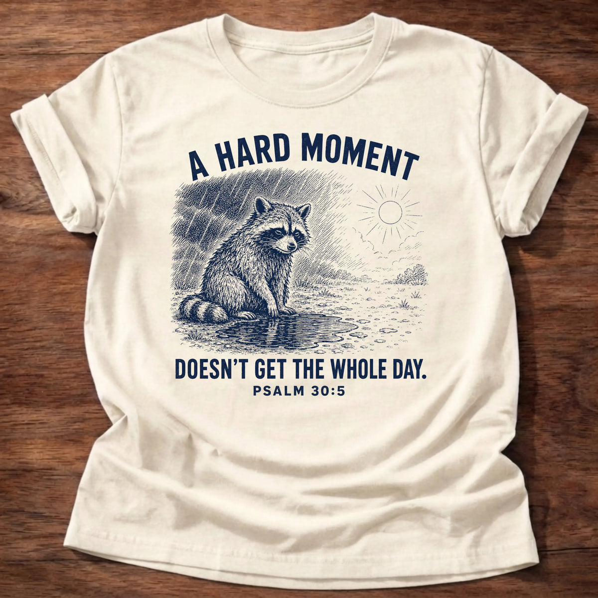 Natural Gildan 64000 t-shirt with a raccoon in the rain illustration and 'A Hard Moment Doesn't Get The Whole Day' text, Psalm 30:5 Christian t-shirt