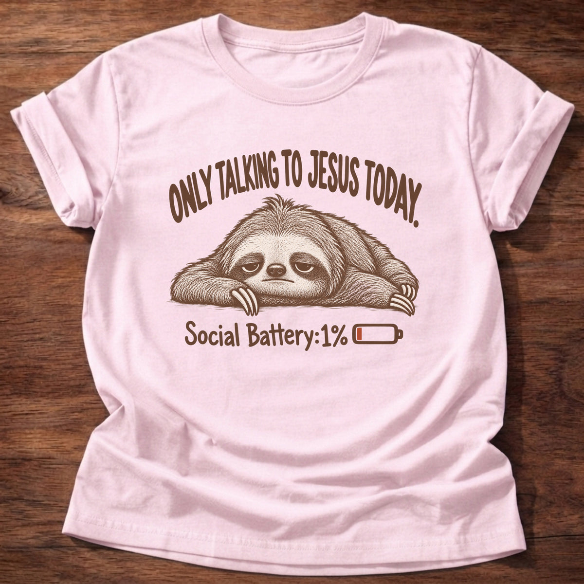 Light Pink t-shirt printed with an exhausted sloth lying flat next to a nearly empty battery icon graphic and “Only talking to Jesus today. Social Battery: 1%” faith based gift