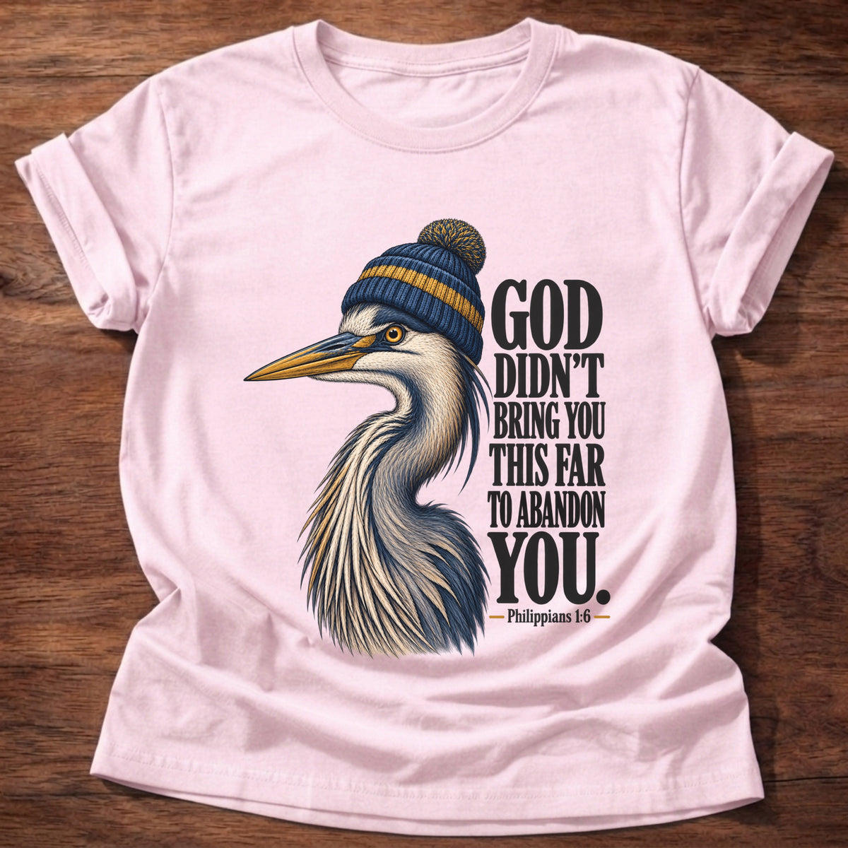 Light Pink t-shirt printed with a great blue heron wearing a knit beanie graphic and “God didn't bring you this far to abandon you.” Philippians 1:6 faith based gift