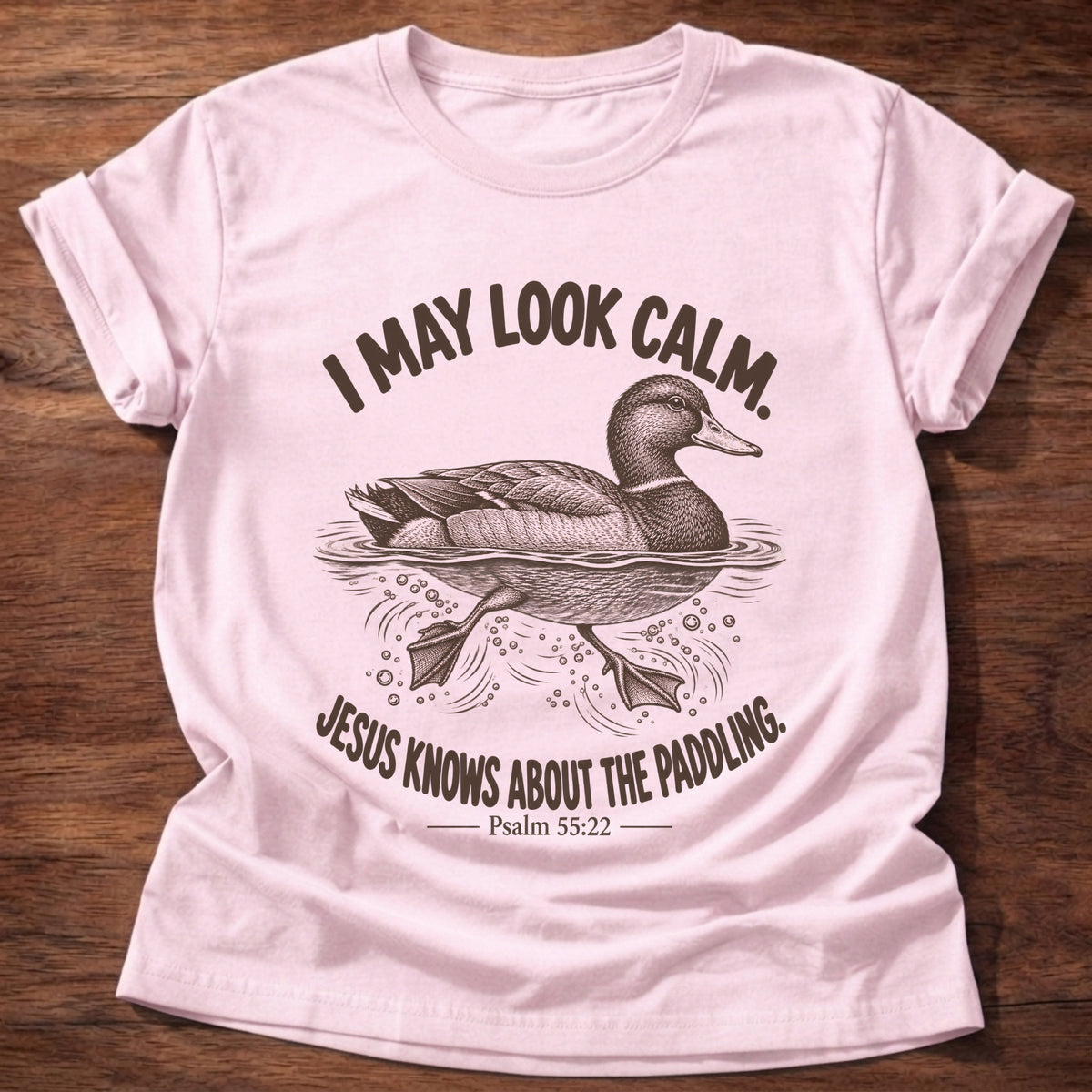 Light Pink t-shirt printed with a mallard duck gliding on the water with its feet paddling underneath graphic and “I may look calm. Jesus knows about the paddling.” Psalm 55:22 faith based gift