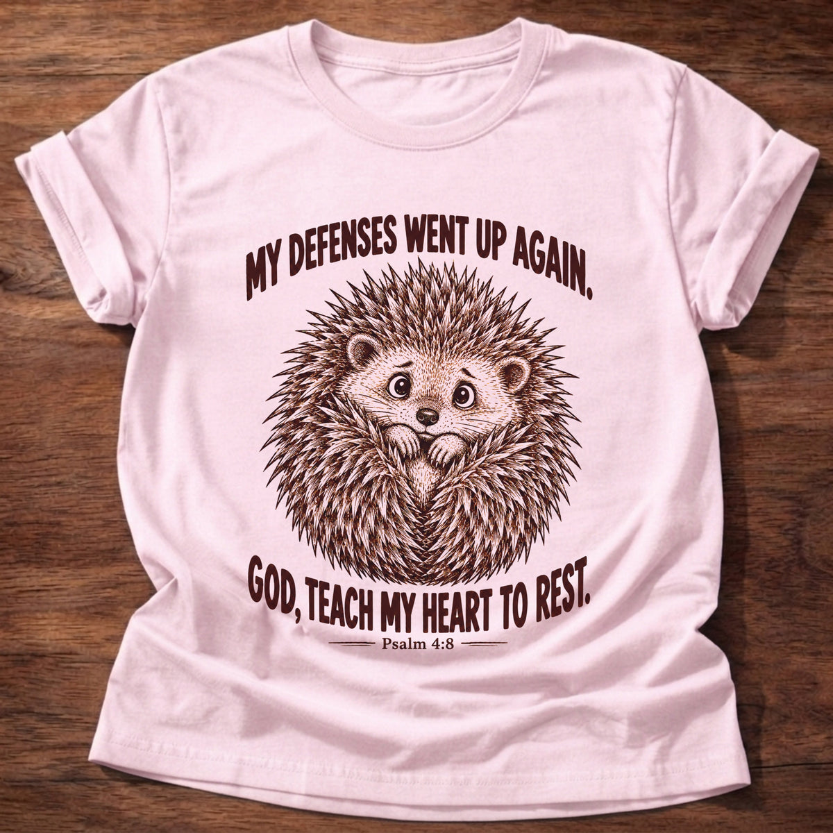 Light Pink t-shirt printed with a worried hedgehog curled up with its quills raised graphic and “My defenses went up again. God, teach my heart to rest.” Psalm 4:8 faith based gift