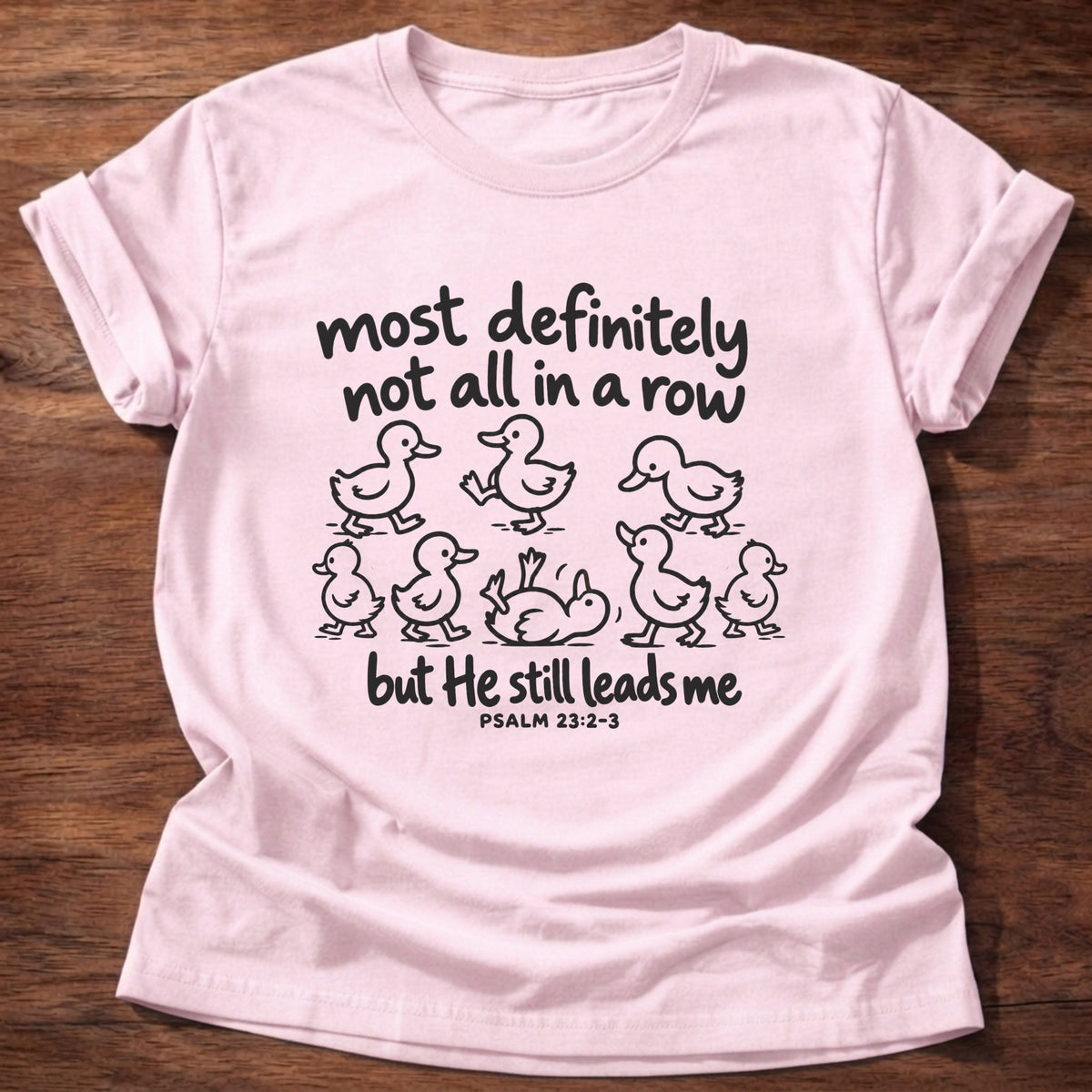 Light Pink t-shirt printed with a scattered line of hand-drawn ducklings graphic and “Most definitely not all in a row, but He still leads me.” Psalm 23:2-3 Christian shirt