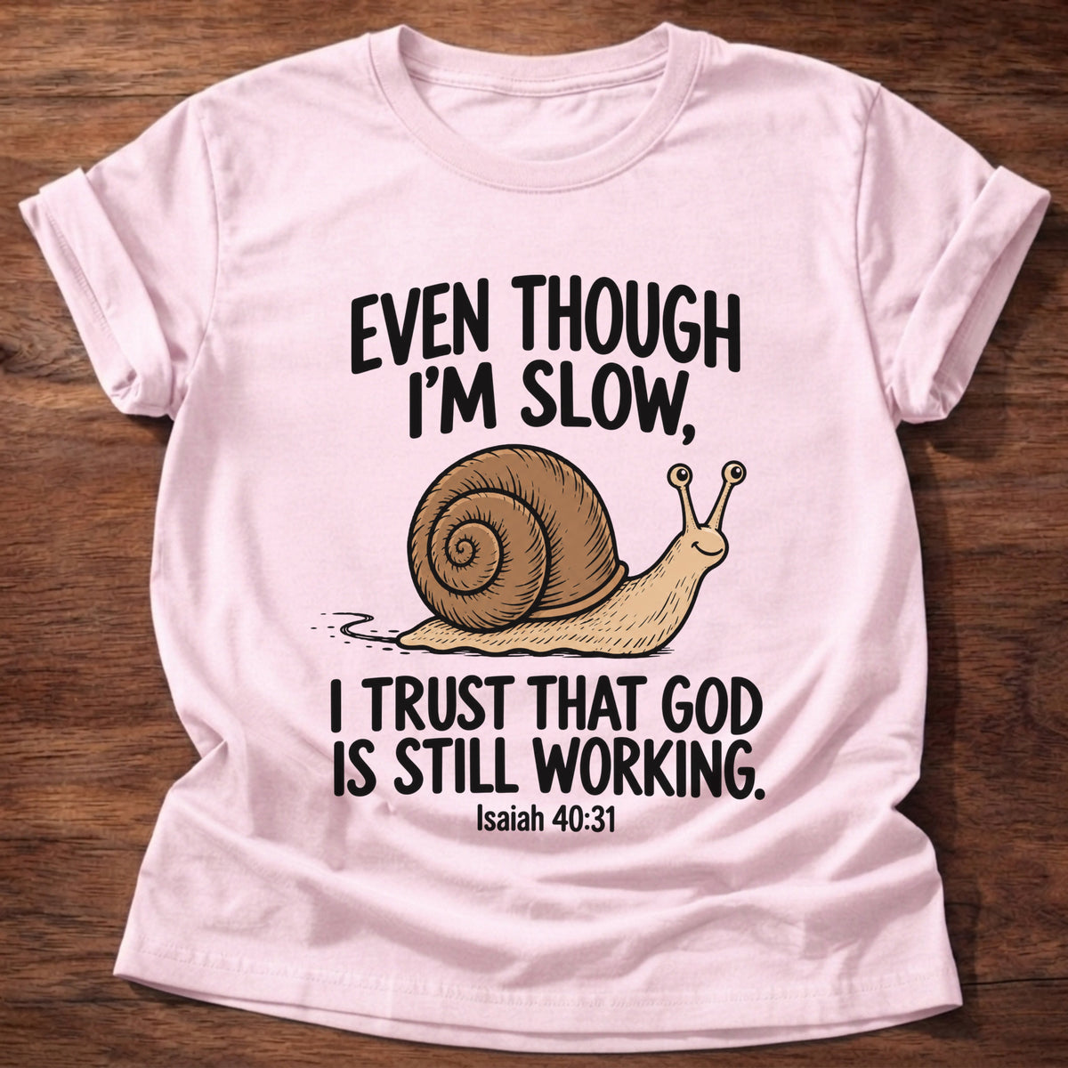 Light Pink t-shirt printed with a snail graphic and 'Even though I'm slow. I trust that God is still working.' Isaiah 40:31 faith based gift