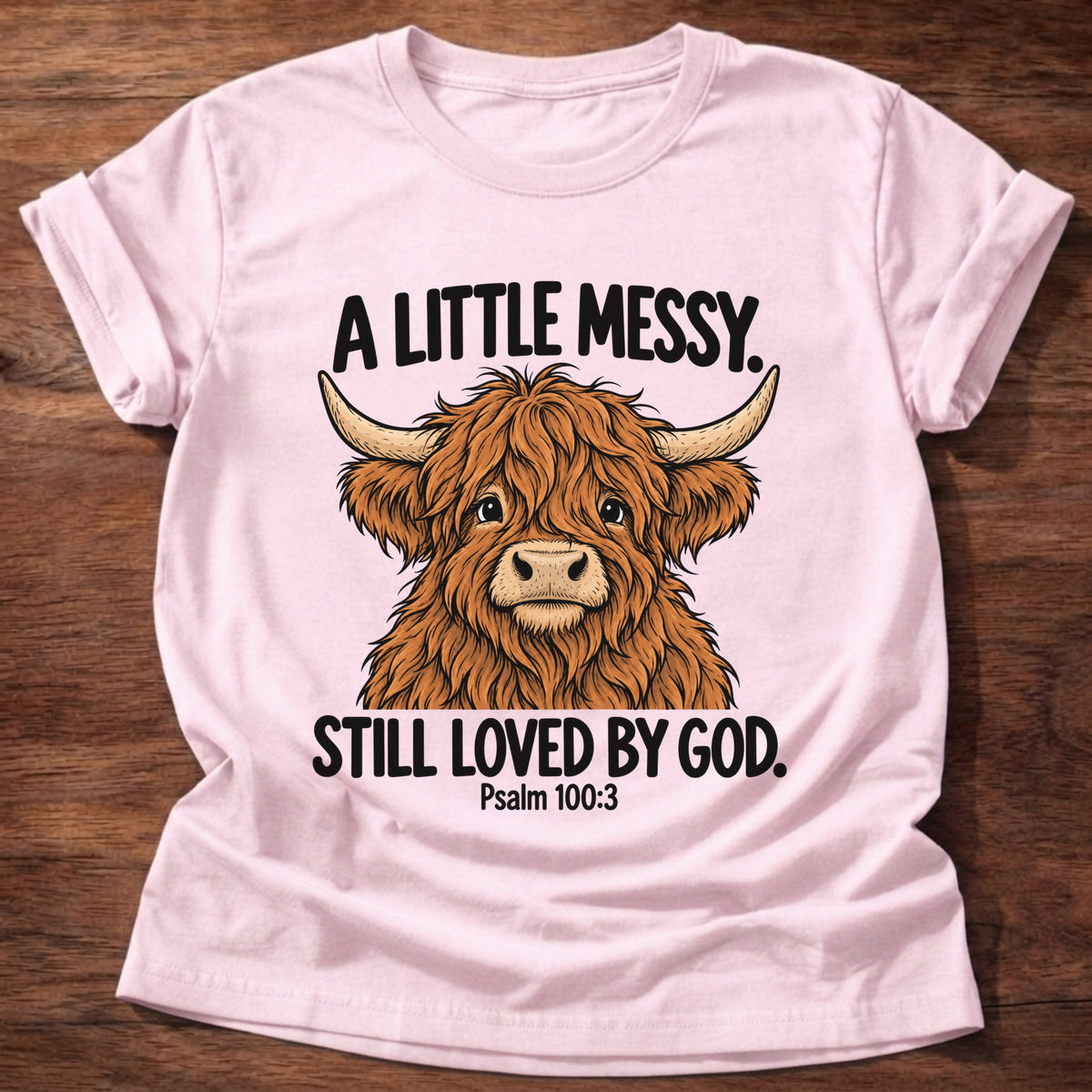 Light Pink t-shirt printed with a highland cow graphic and 'A little messy. Still loved by God.' Psalm 100:3 faith based gift