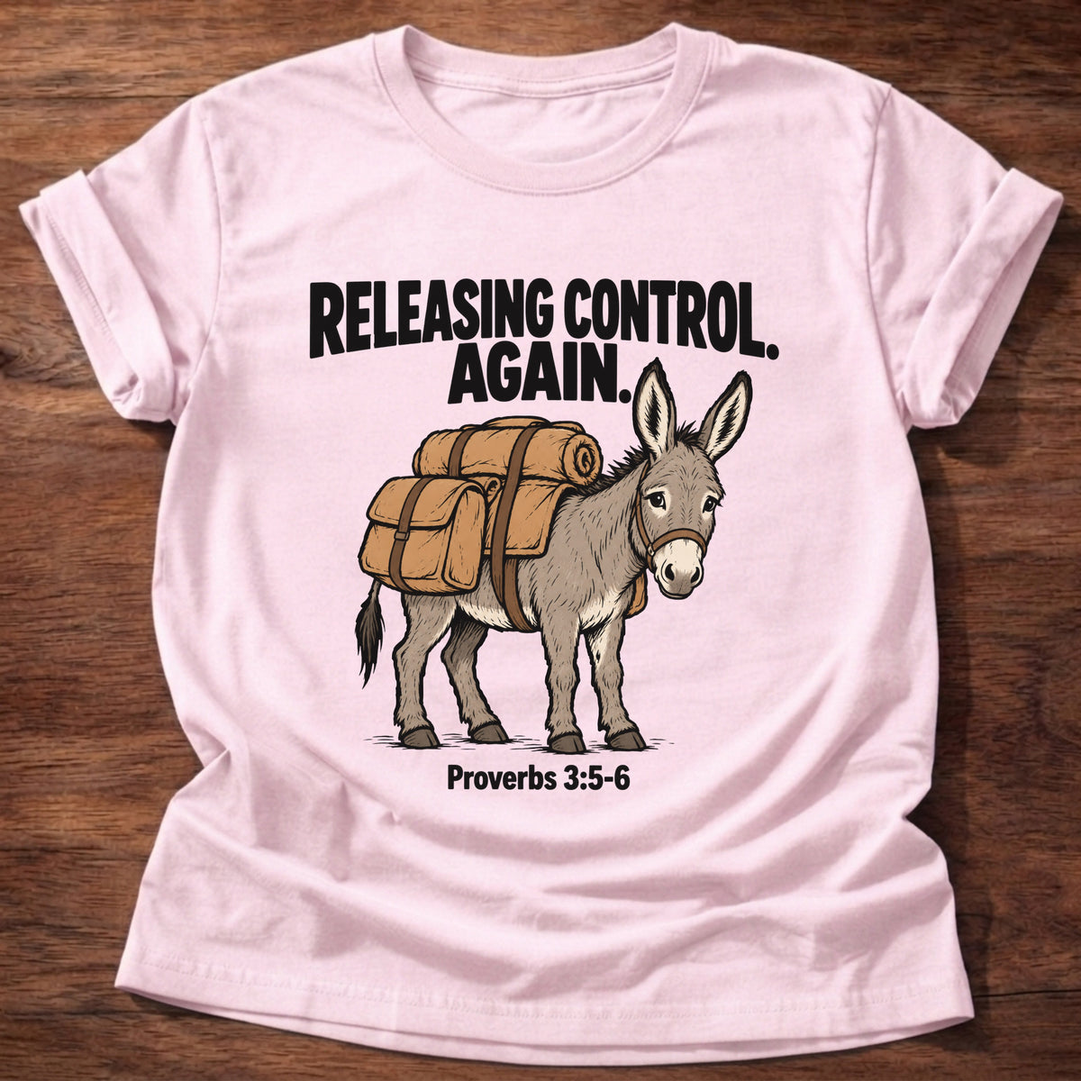 Light Pink t-shirt printed with a donkey carrying a backpack graphic and 'Releasing control. Again.' Proverbs 3:5-6 faith based gift