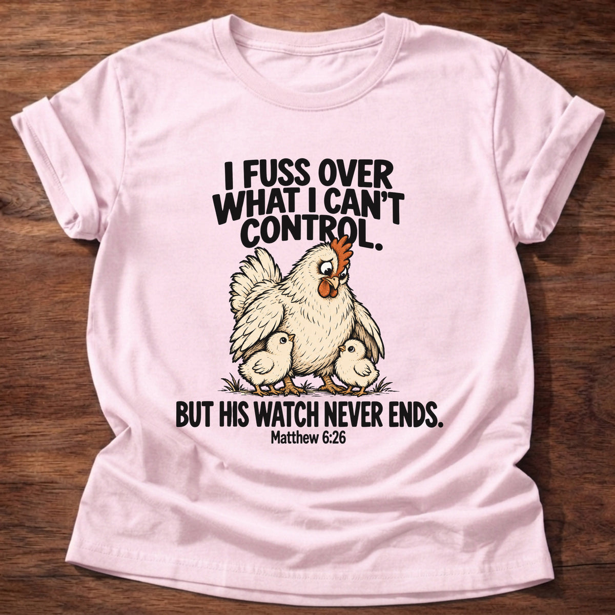 Light Pink t-shirt printed with a fussing hen graphic and 'I fuss over what I can't control. But His watch never ends.' Matthew 6:26 faith based gift