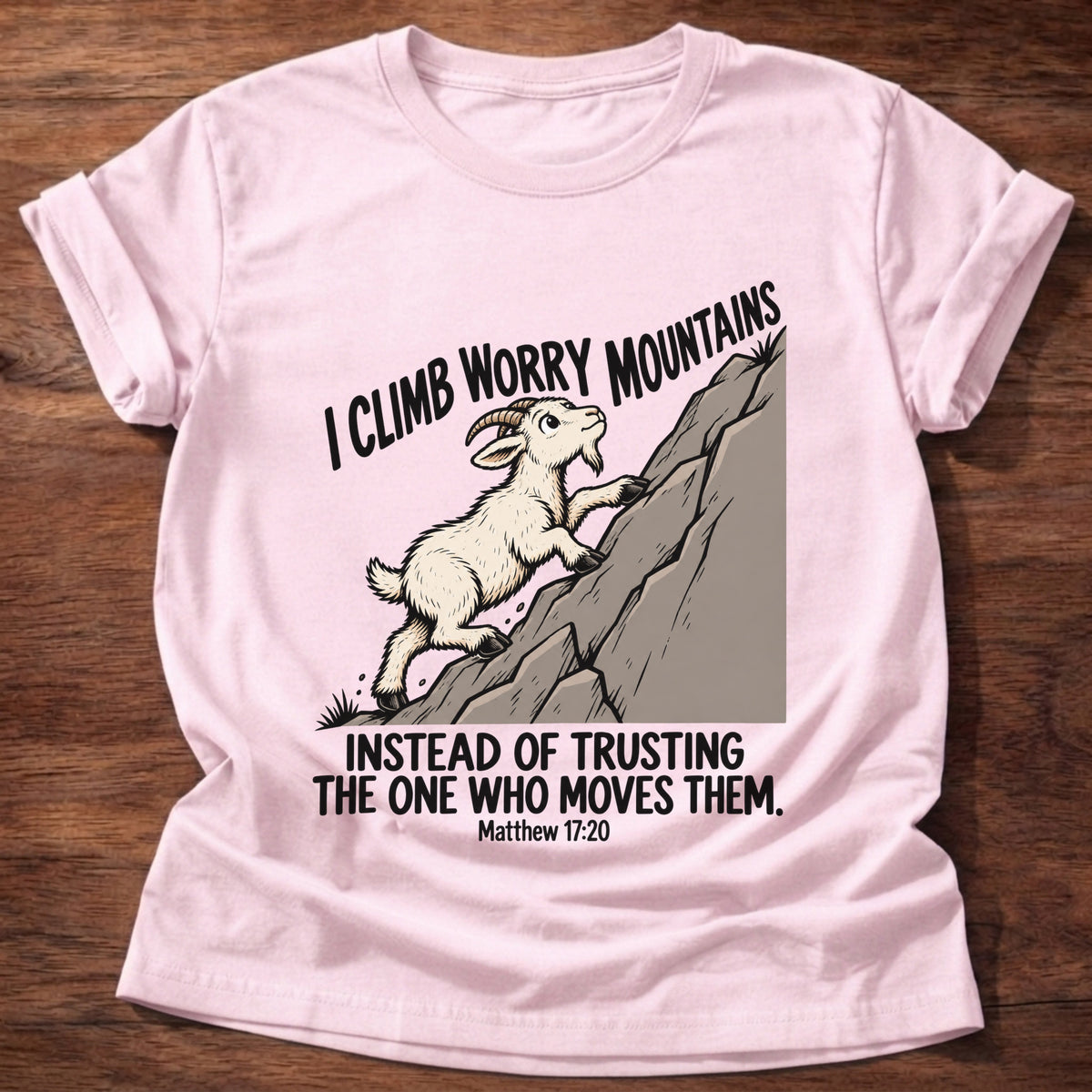 Light Pink t-shirt printed with a goat climbing a mountain graphic and 'I climb worry mountains instead of trusting the One who moves them.' Matthew 17:20 faith based gift