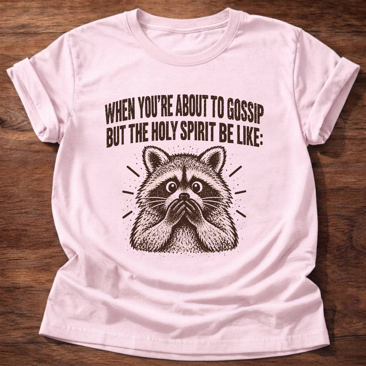 Light Pink t-shirt printed with a startled raccoon graphic and 'When you're about to gossip but the Holy Spirit be like.' Proverbs 16:28 faith based gift