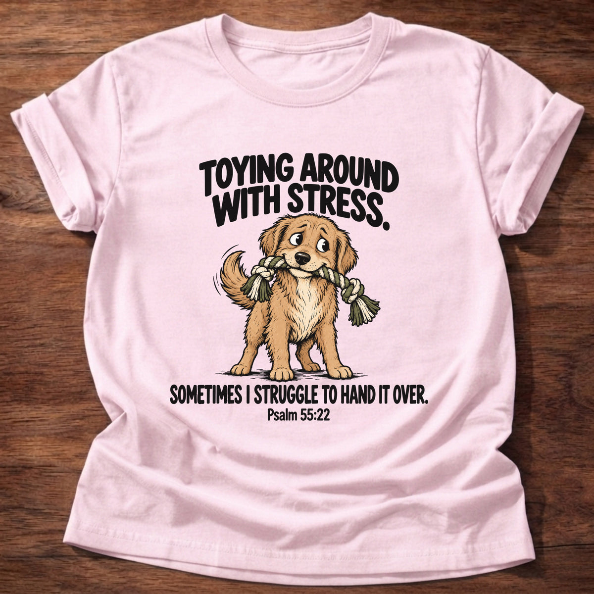 Light Pink t-shirt printed with a dog tugging a rope toy graphic and 'Toying around with stress. Sometimes I struggle to hand it over.' Psalm 55:22 faith based gift