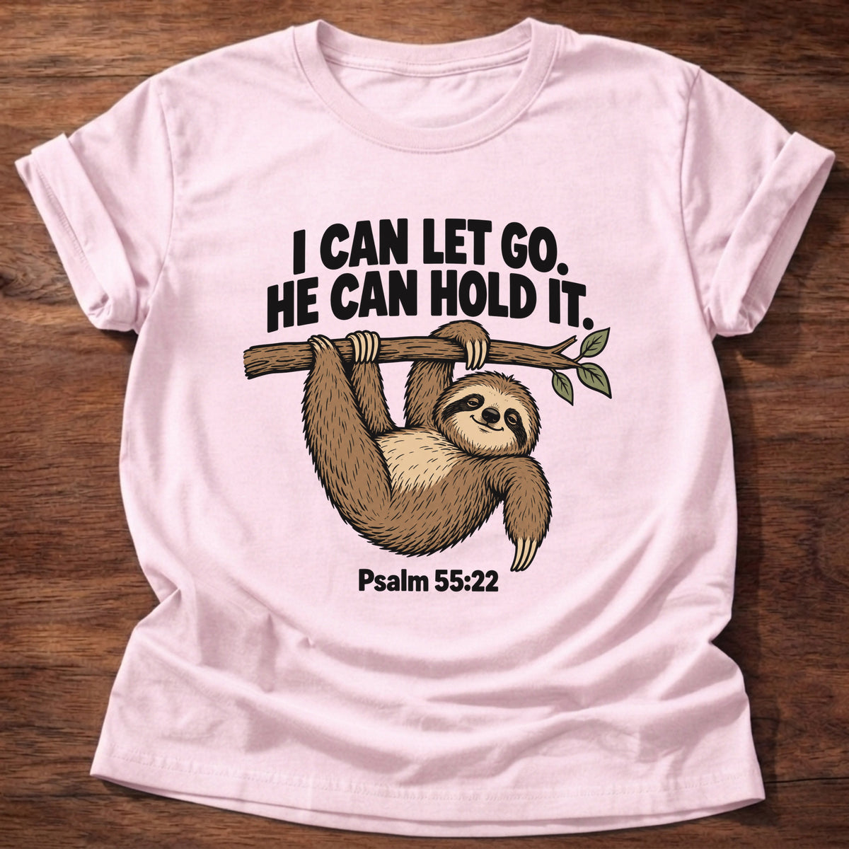 Light Pink t-shirt printed with a sloth hanging from a branch graphic and 'I can let go. He can hold it.' Psalm 55:22 faith based gift