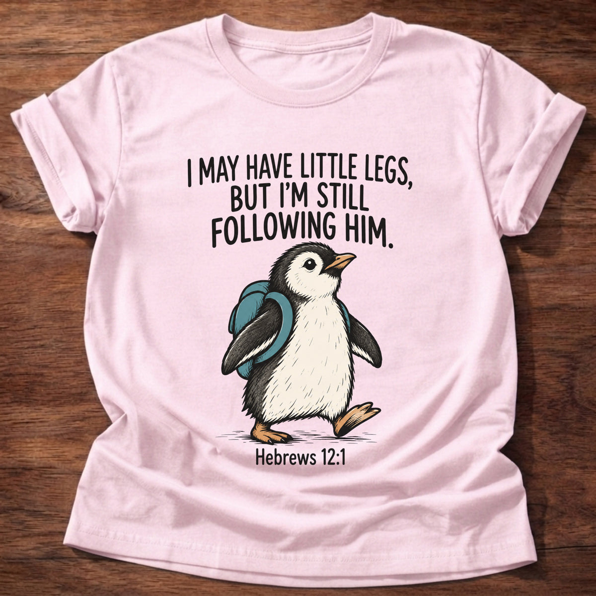 Light Pink t-shirt printed with a penguin graphic and 'I may have little legs, but I'm still following Him.' Hebrews 12:1 faith based gift