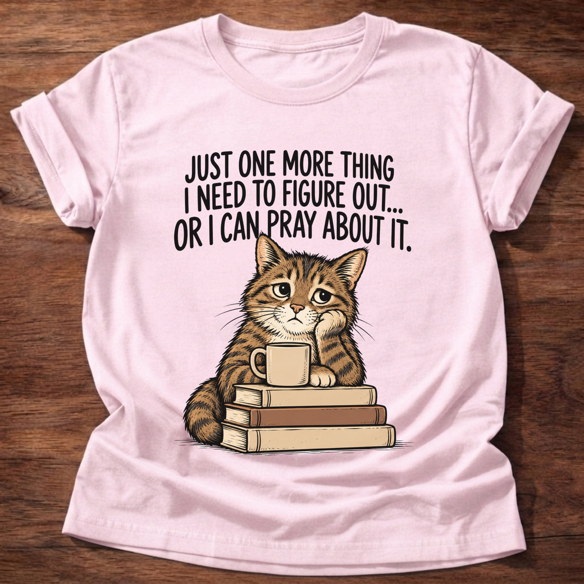 Light Pink t-shirt printed with a cat surrounded by books graphic and 'Just one more thing I need to figure out... or I can pray about it.' Philippians 4:6-7 faith based gift