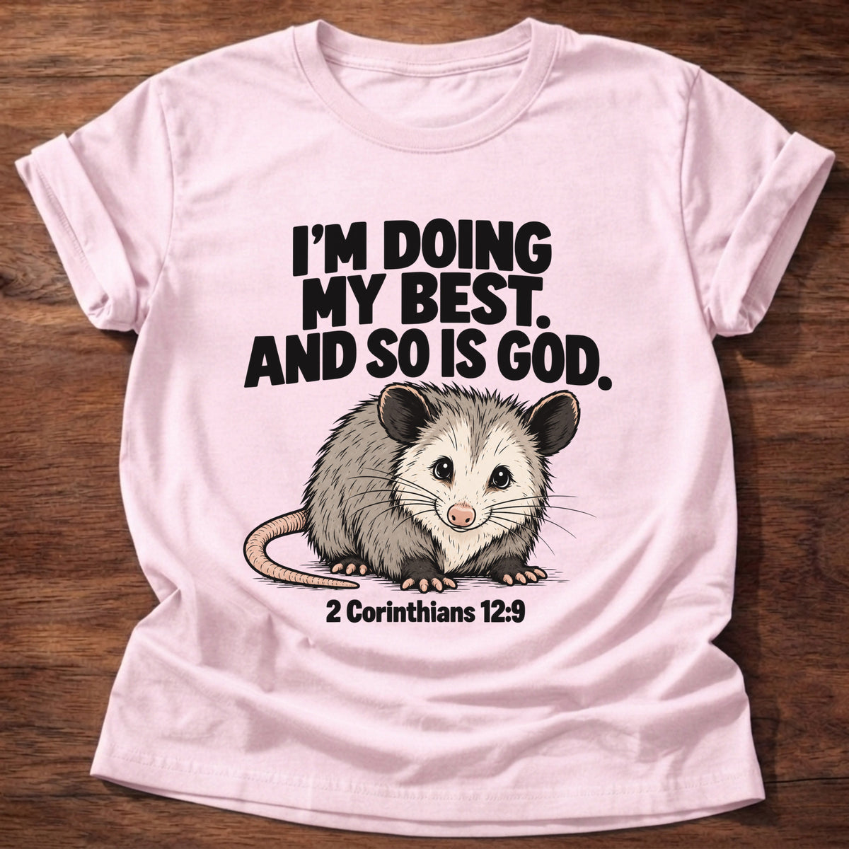 Light Pink t-shirt printed with an opossum graphic and 'I'm doing my best. And so is God.' 2 Corinthians 12:9 faith based gift