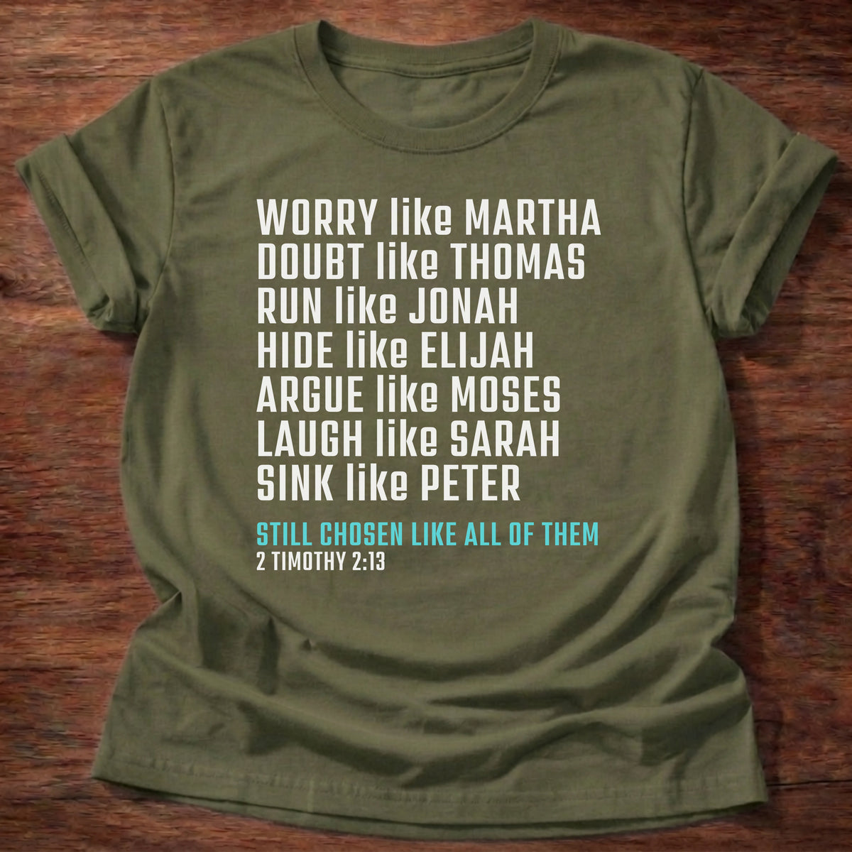 Military Green t-shirt printed with bold stacked typography listing Bible characters graphic and “Worry like Martha. Doubt like Thomas. Sink like Peter. Still chosen like all of them.” 2 Timothy 2:13 Christian shirt