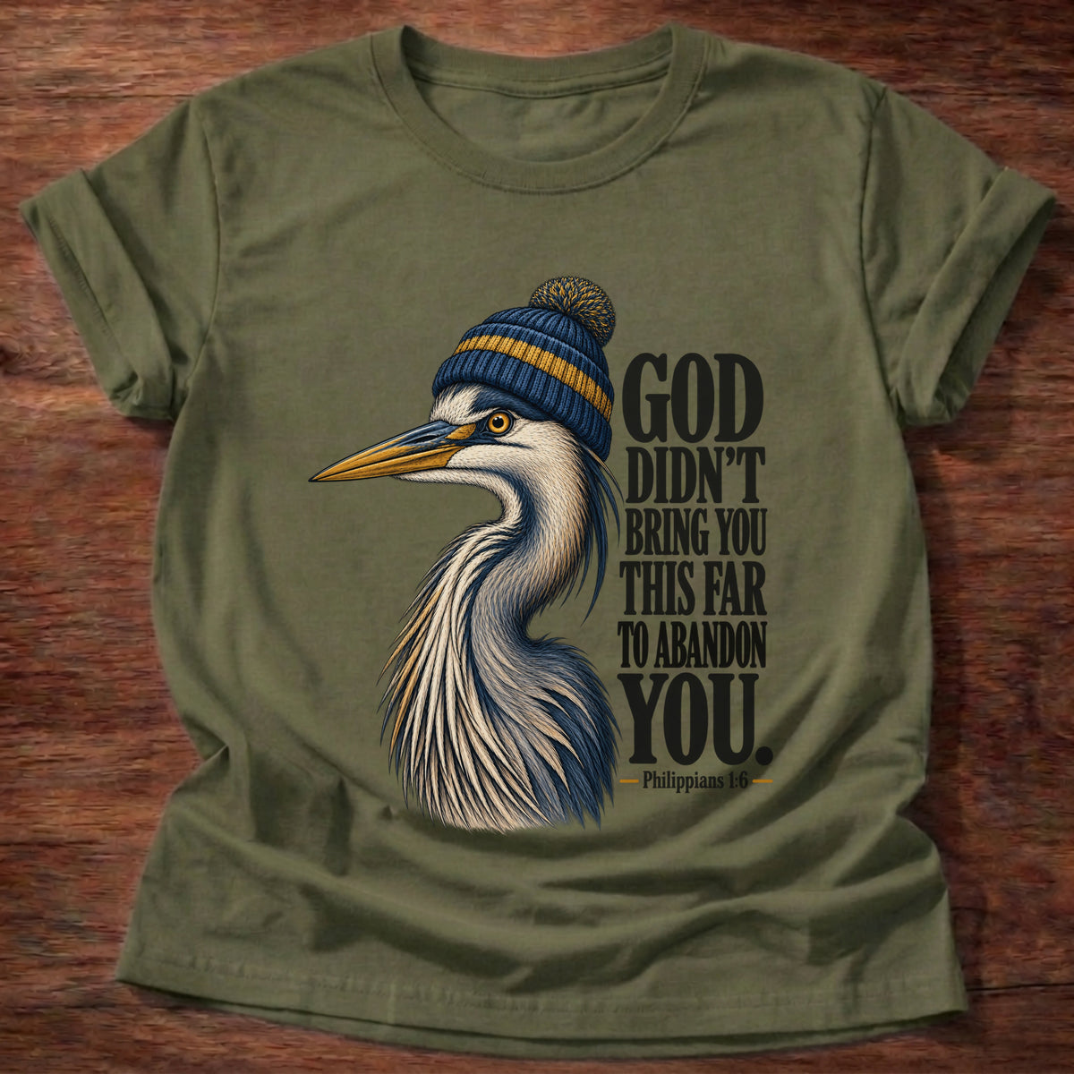 Military Green t-shirt printed with a great blue heron wearing a knit beanie graphic and “God didn't bring you this far to abandon you.” Philippians 1:6 faith based gift