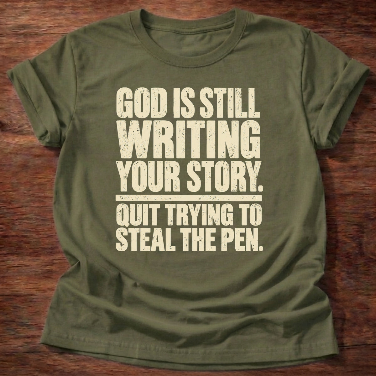 Military Green t-shirt printed with bold stacked typography graphic and “God is still writing your story. Quit trying to steal the pen.” Philippians 1:6 Christian shirt