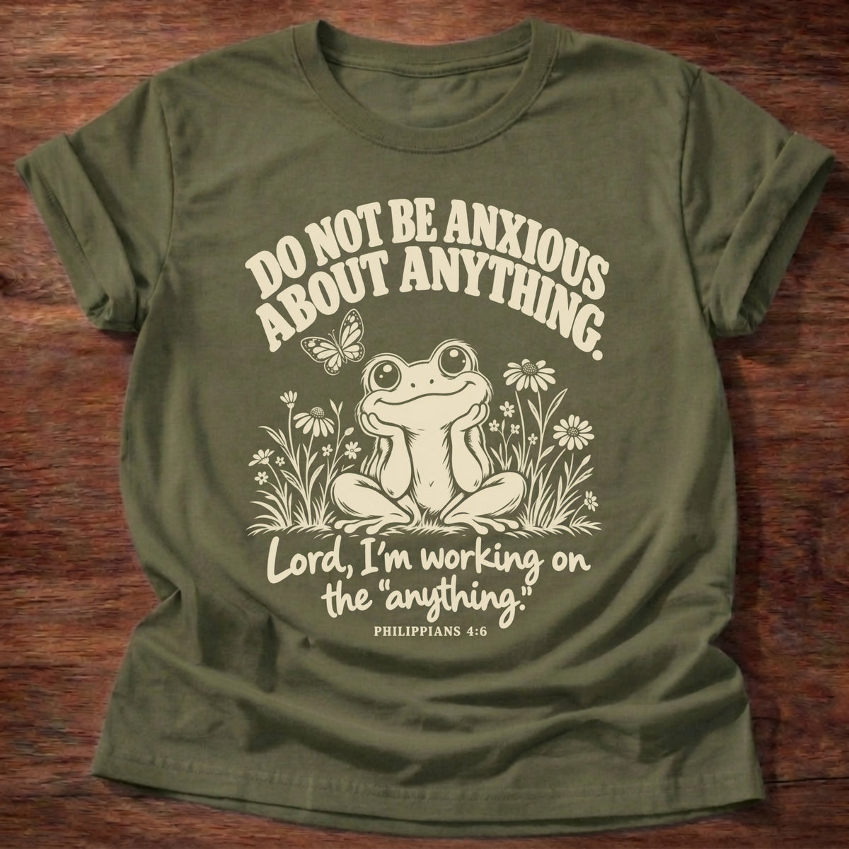 Anything Part T-Shirt in Military Green featuring a wide-eyed frog sitting among wildflowers and Philippians 4:6 anxiety humor design