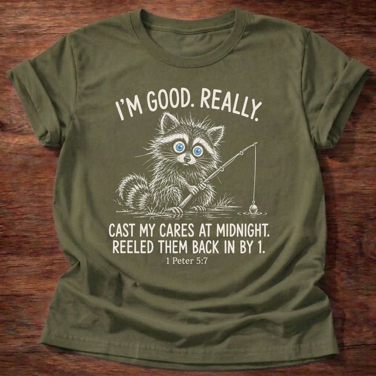 Military Green t-shirt printed with a raccoon holding a fishing rod graphic and “I'm good. Really. Cast my cares at midnight. Reeled them back in by 1.” 1 Peter 5:7 Christian shirt