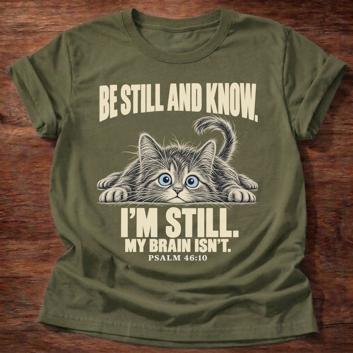 Brain Not Still T-Shirt in Military Green featuring a wide-eyed cat lying flat with alert eyes and Psalm 46:10 overthinking humor design