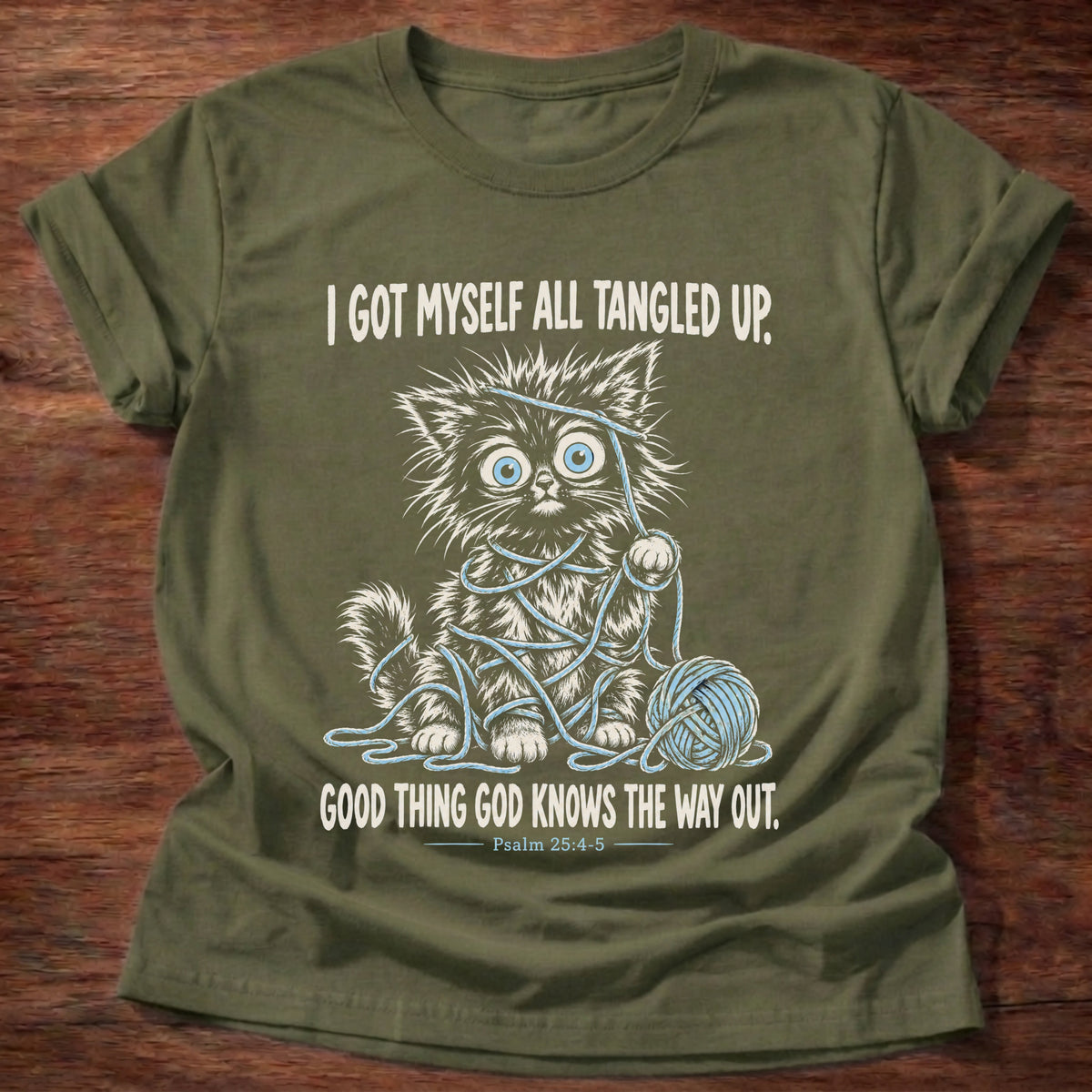 Military Green t-shirt printed with a wide-eyed kitten tangled up in blue yarn next to a yarn ball graphic and “I got myself all tangled up. Good thing God knows the way out.” Psalm 25:4-5 faith based gift