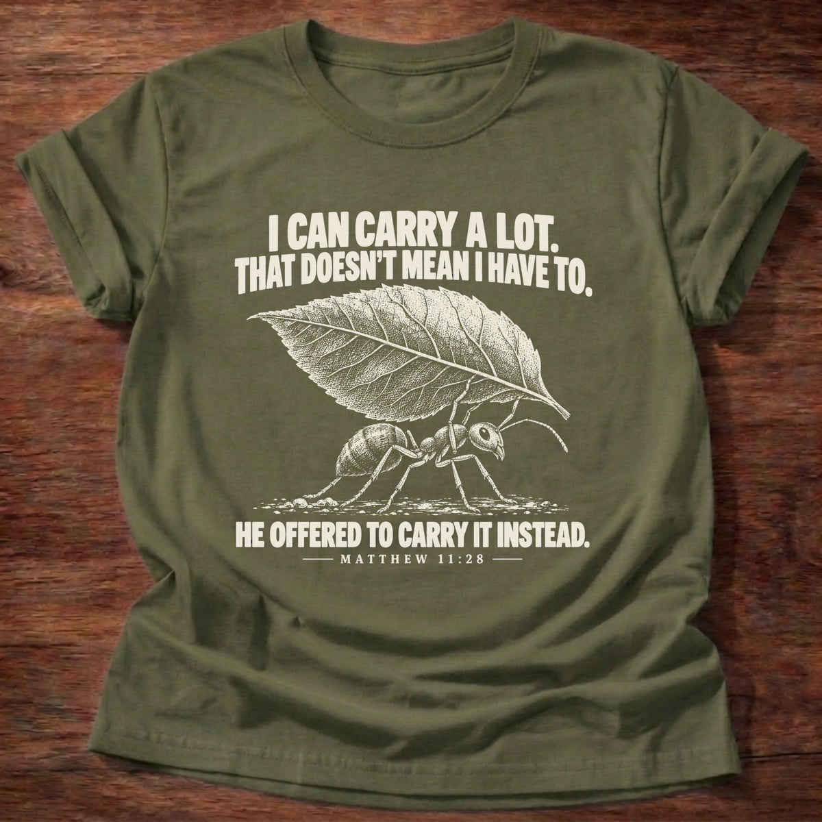 Military Green t-shirt printed with an ant hauling a leaf many times its size graphic and 'I can carry a lot. That doesn't mean I have to. He offered to carry it instead.' Matthew 11:28 faith based gift