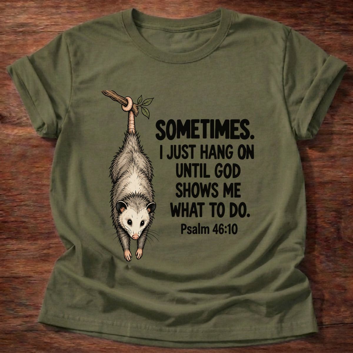 Military Green t-shirt printed with a possum hanging by its tail graphic and 'Sometimes. I just hang on until God shows me what to do.' Psalm 46:10 faith based gift
