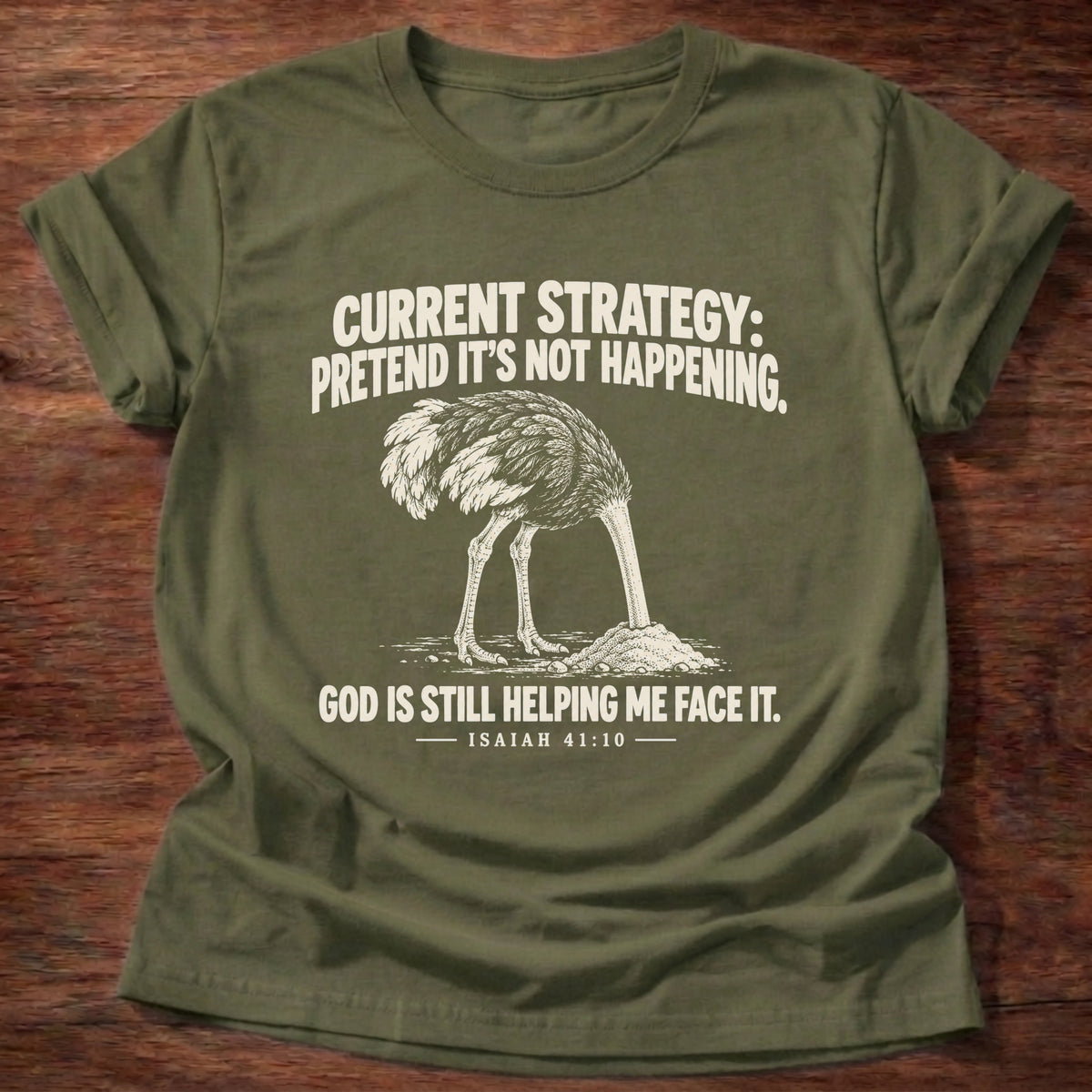 Military Green t-shirt printed with an ostrich with its head buried in the sand graphic and 'Current strategy: pretend it's not happening. God is still helping me face it.' Isaiah 41:10 faith based gift