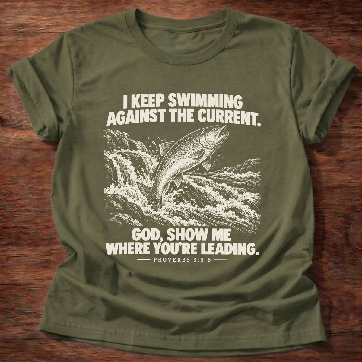 Military Green t-shirt printed with a fish leaping against a rushing current graphic and 'I keep swimming against the current. God, show me where you're leading.' Proverbs 3:5-6 faith based gift