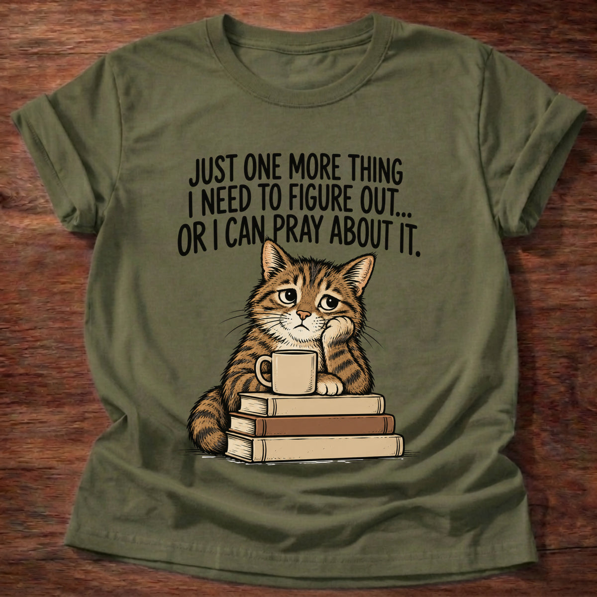 Military Green t-shirt printed with a cat surrounded by books graphic and 'Just one more thing I need to figure out... or I can pray about it.' Philippians 4:6-7 faith based gift