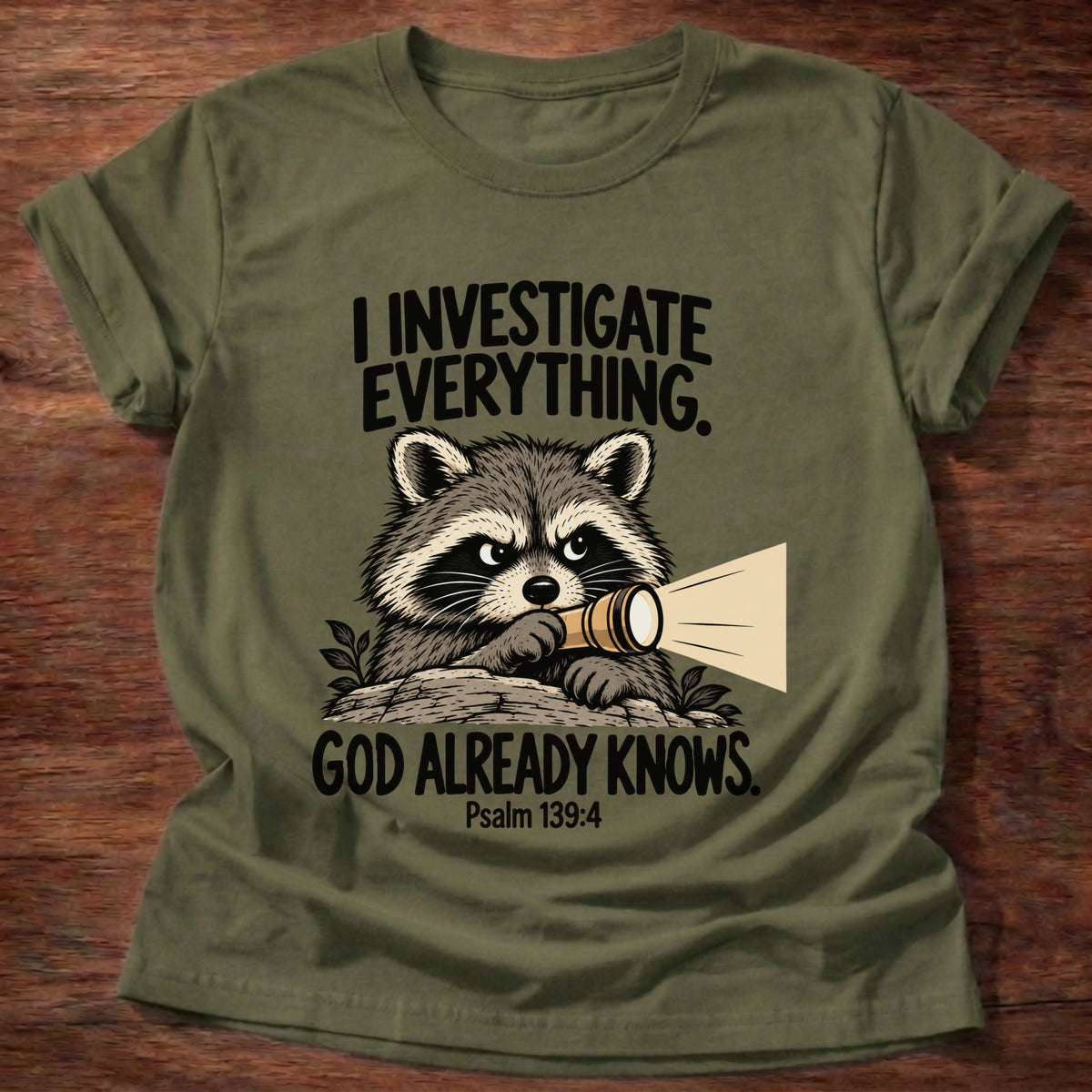 Military Green t-shirt printed with a raccoon holding a magnifying glass graphic and 'I investigate everything. God already knows.' Psalm 139:4 faith based gift